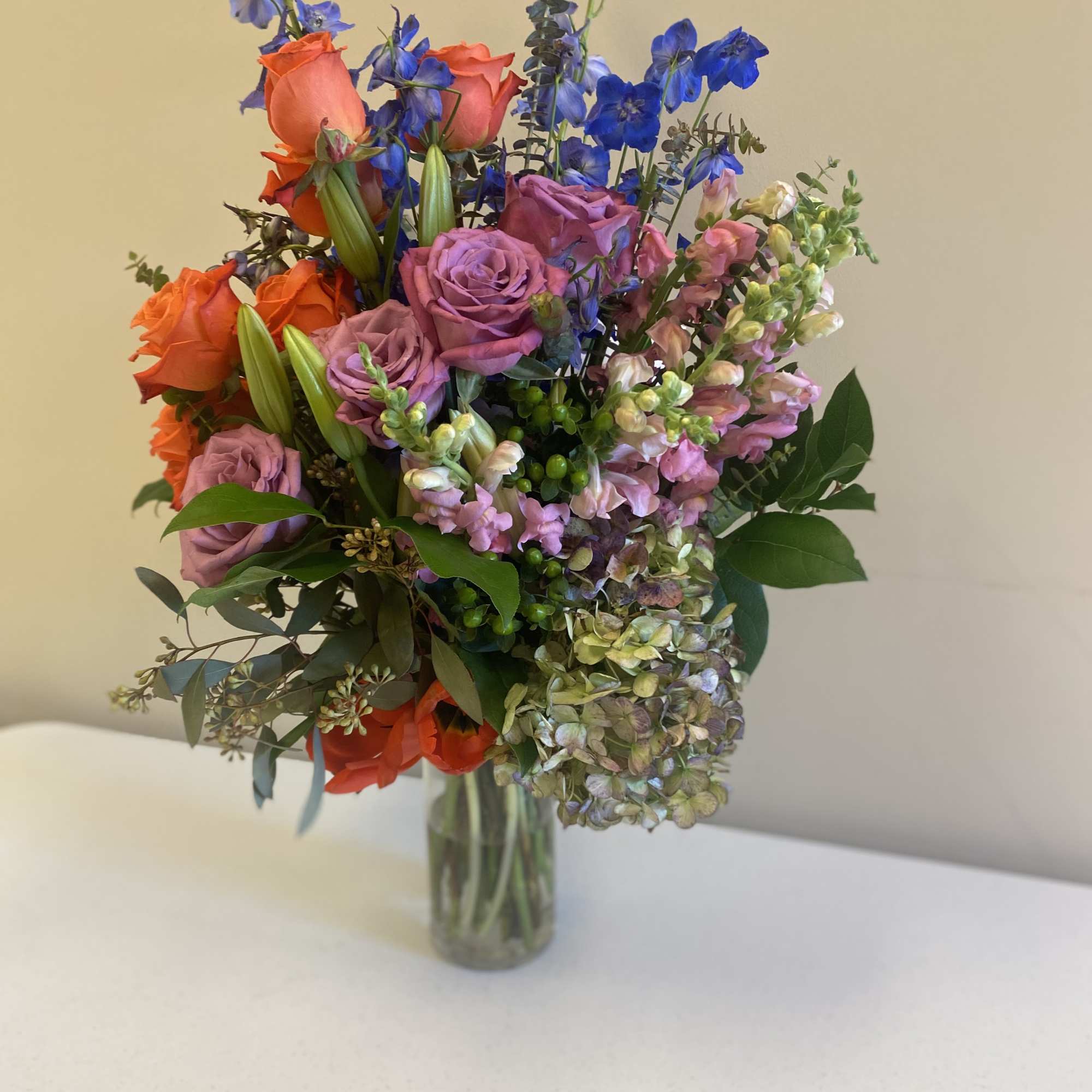 Mixed bouquet of roses, lilies, and blue delphinium in a glass vase