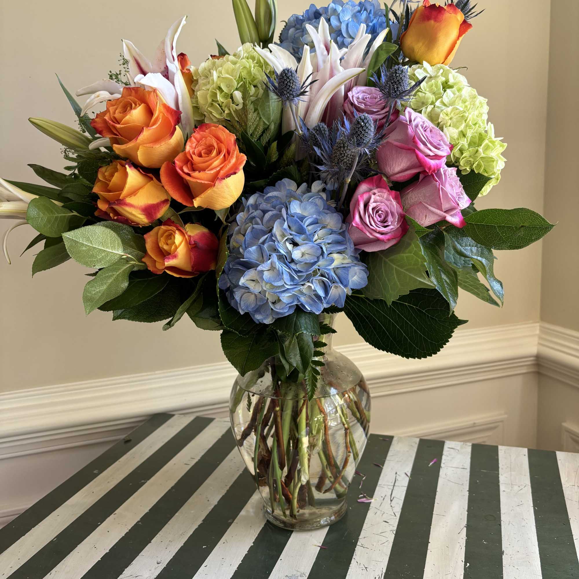 Colorful bouquet of roses, hydrangeas, and lilies in a clear glass vase