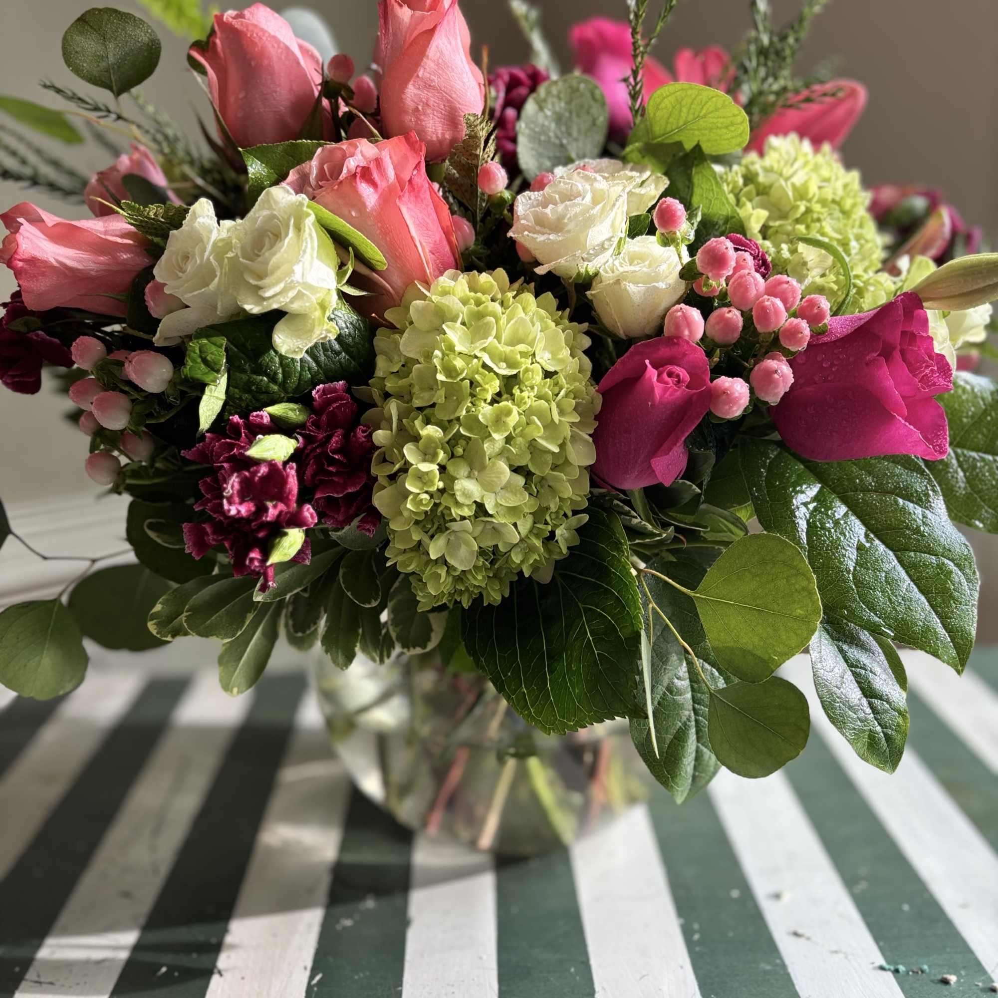Pink and white roses with green hydrangea in a glass vase