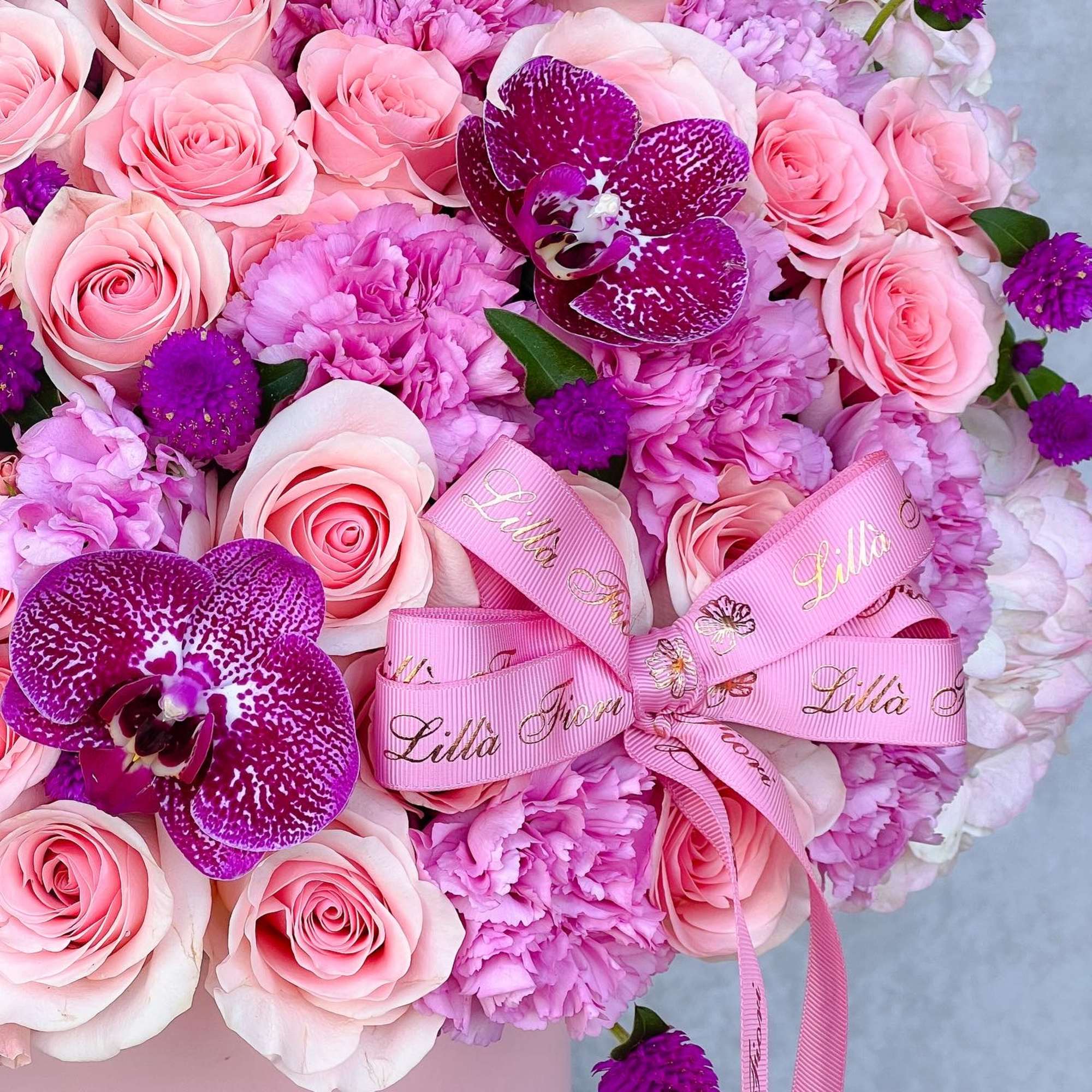 Pink roses and purple orchids arranged with pink ribbon