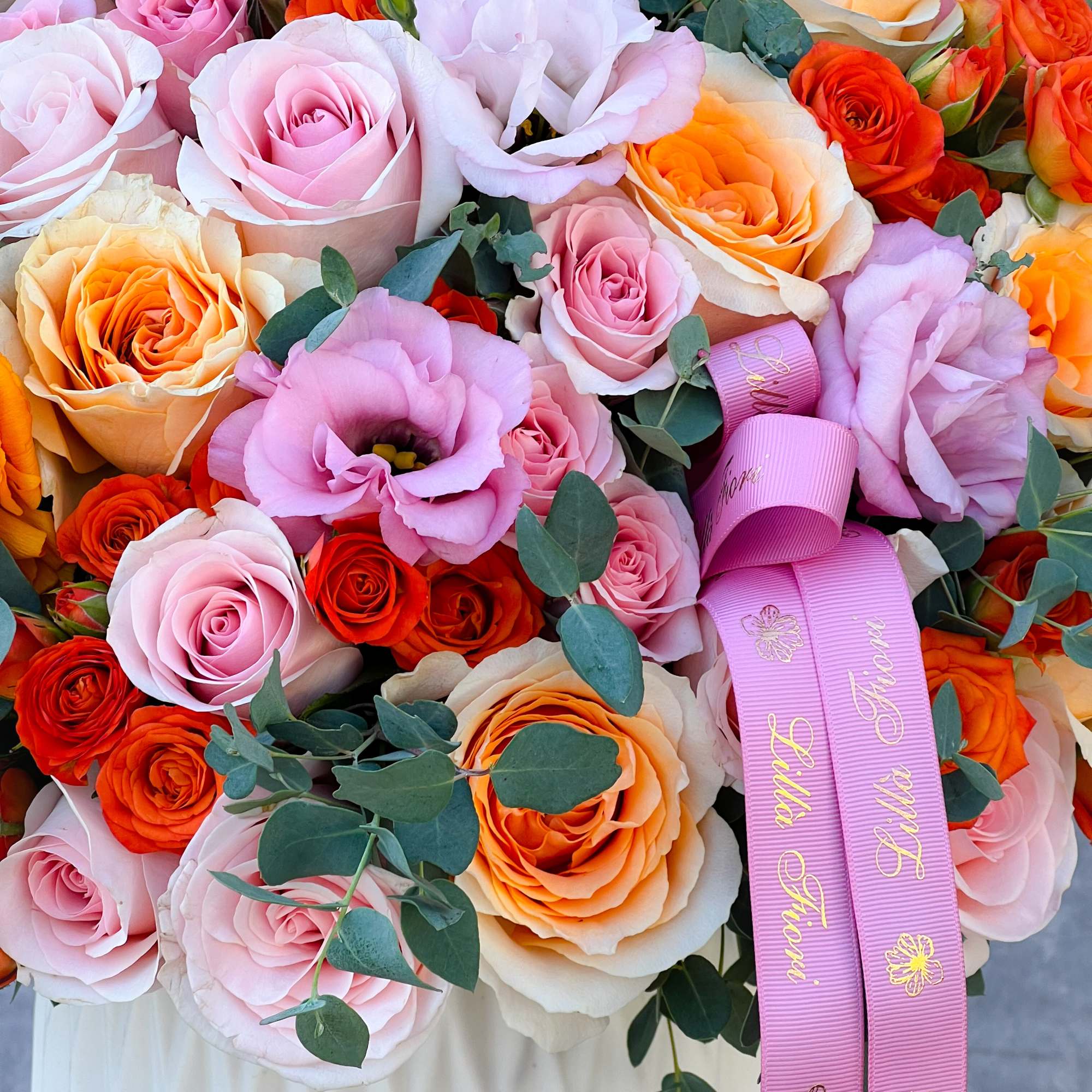 Bouquet of pink, peach, and orange roses with lavender blooms and ribbon