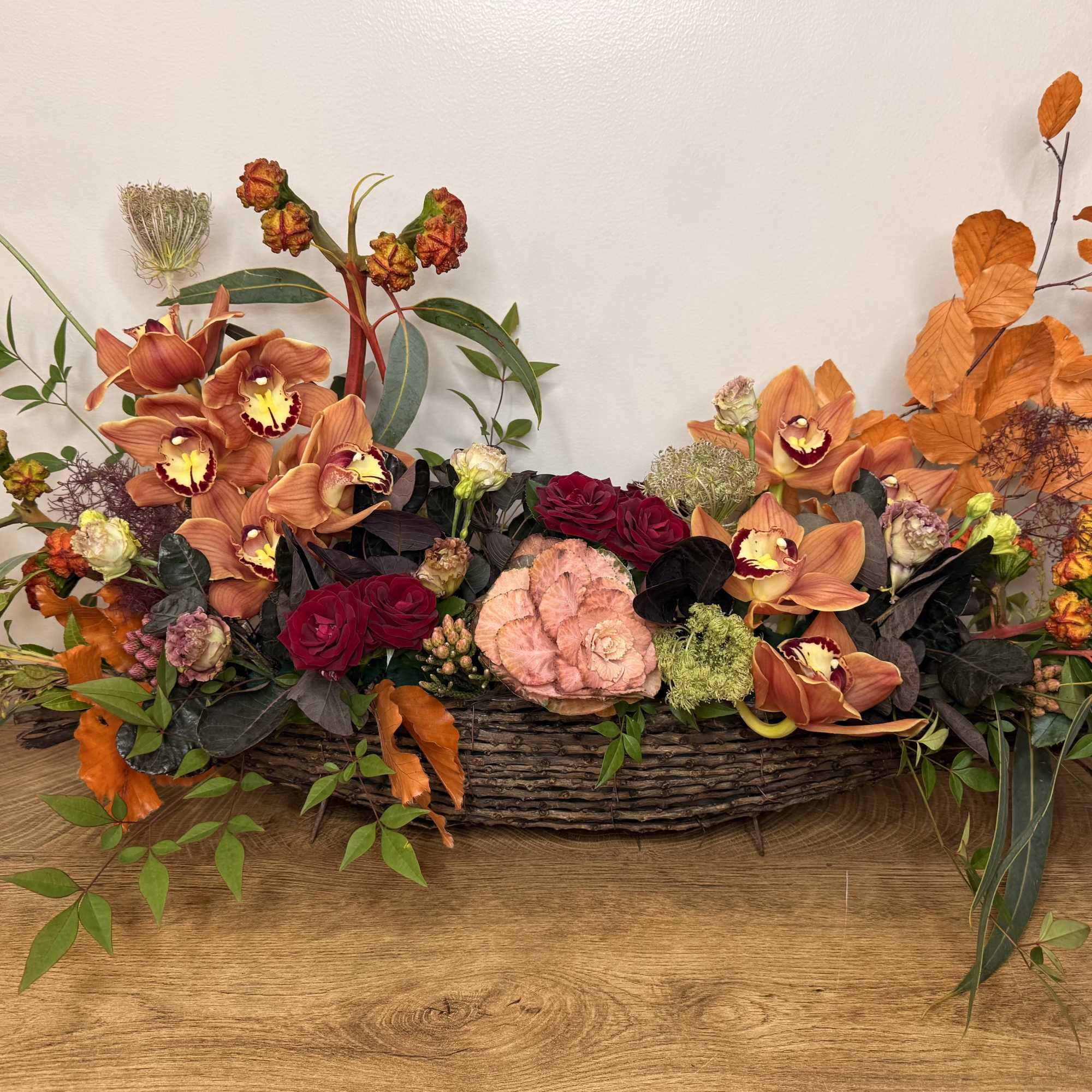 Low floral centerpiece in a woven basket with orange orchids and red roses