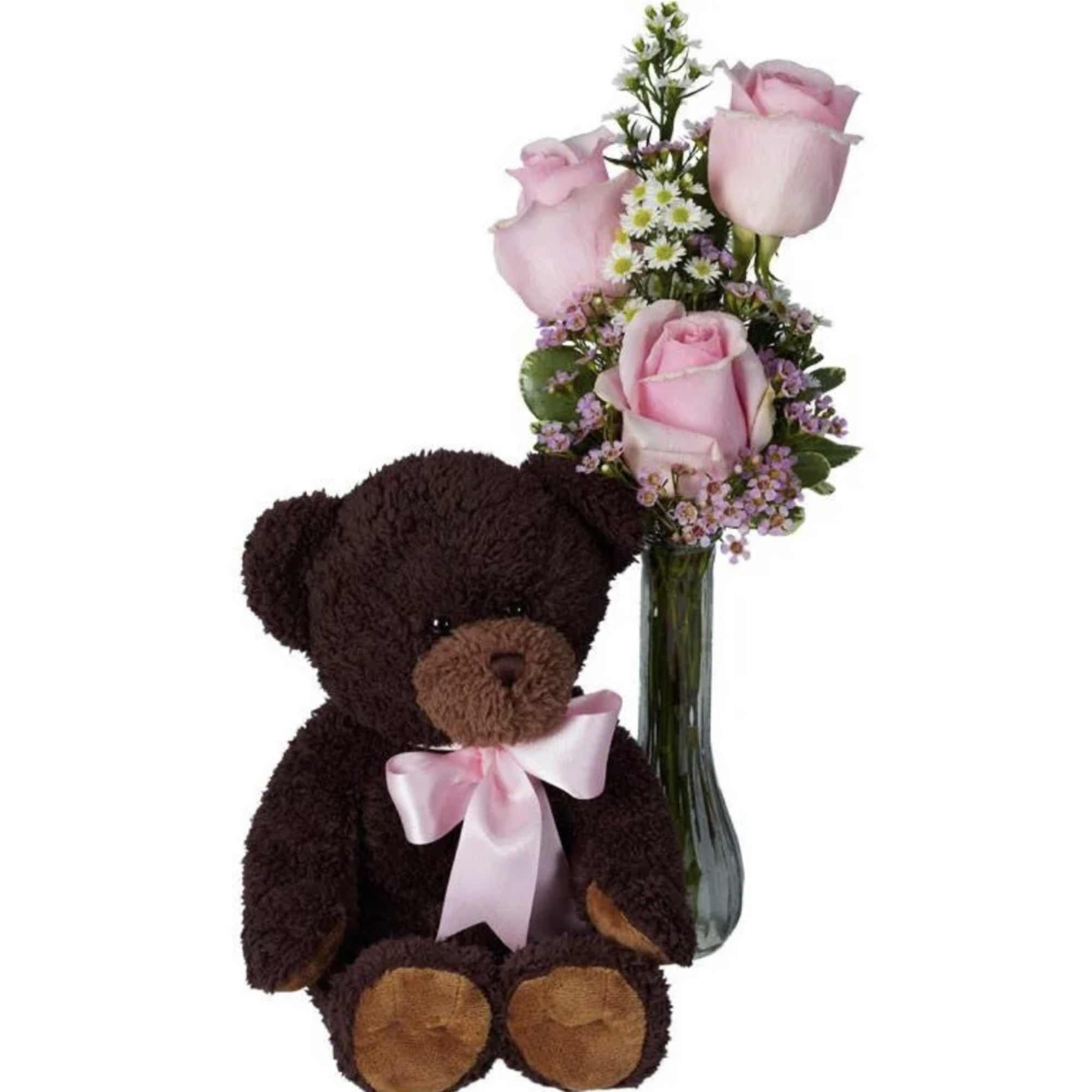 Pink rose bouquet in a glass vase beside a teddy bear with a ribbon