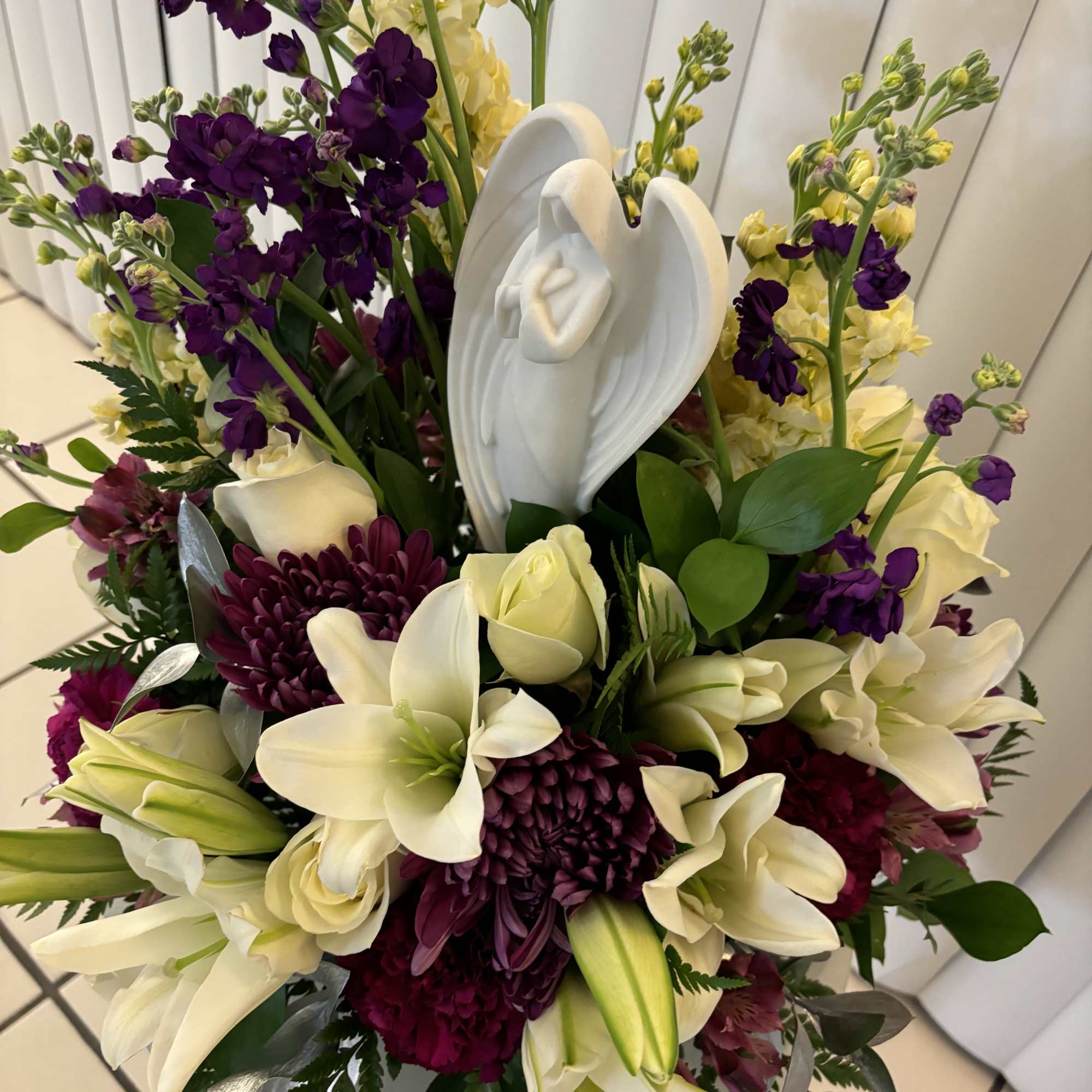 White lilies and purple flowers arranged around a white angel figurine