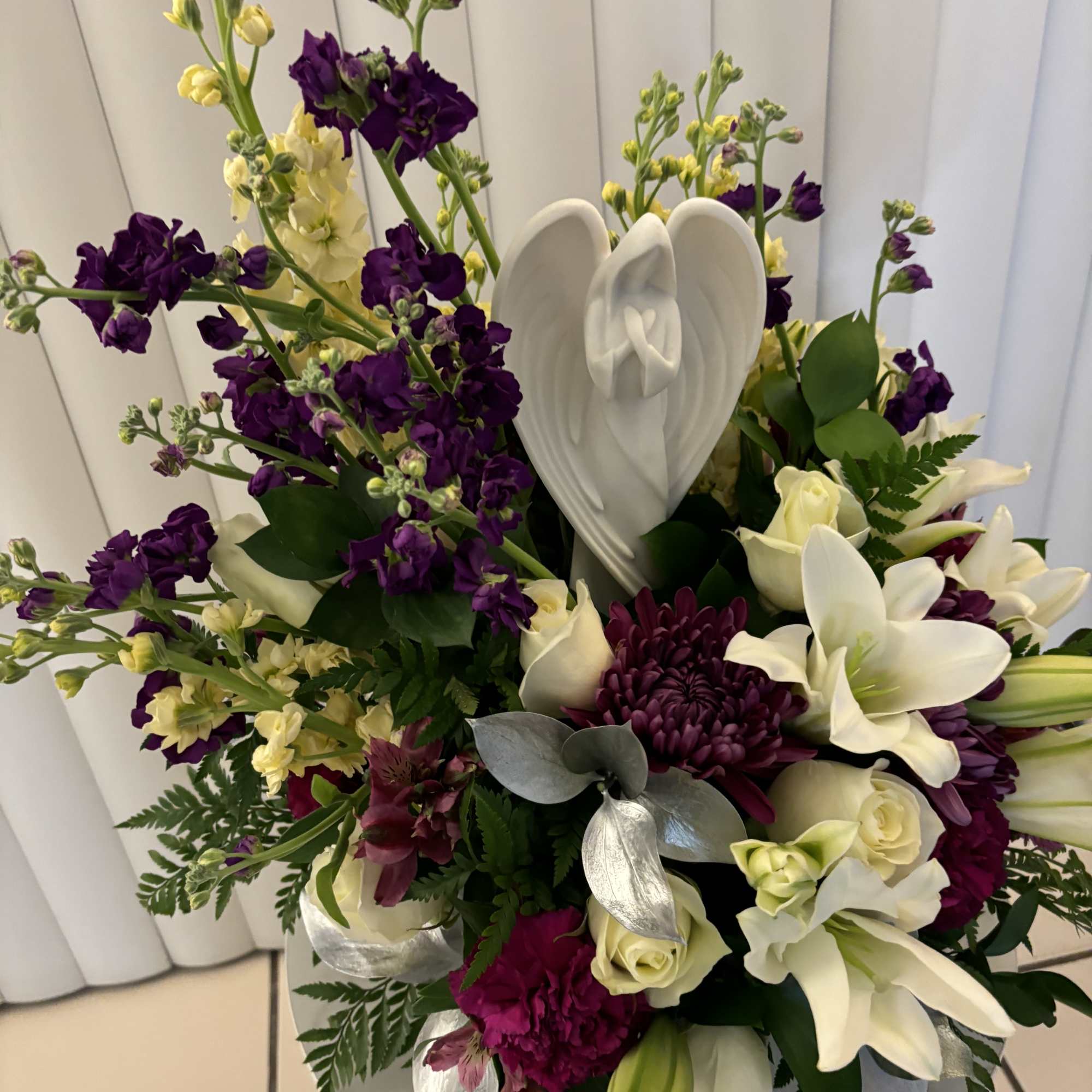 Purple and white floral arrangement with lilies and roses in a white vase