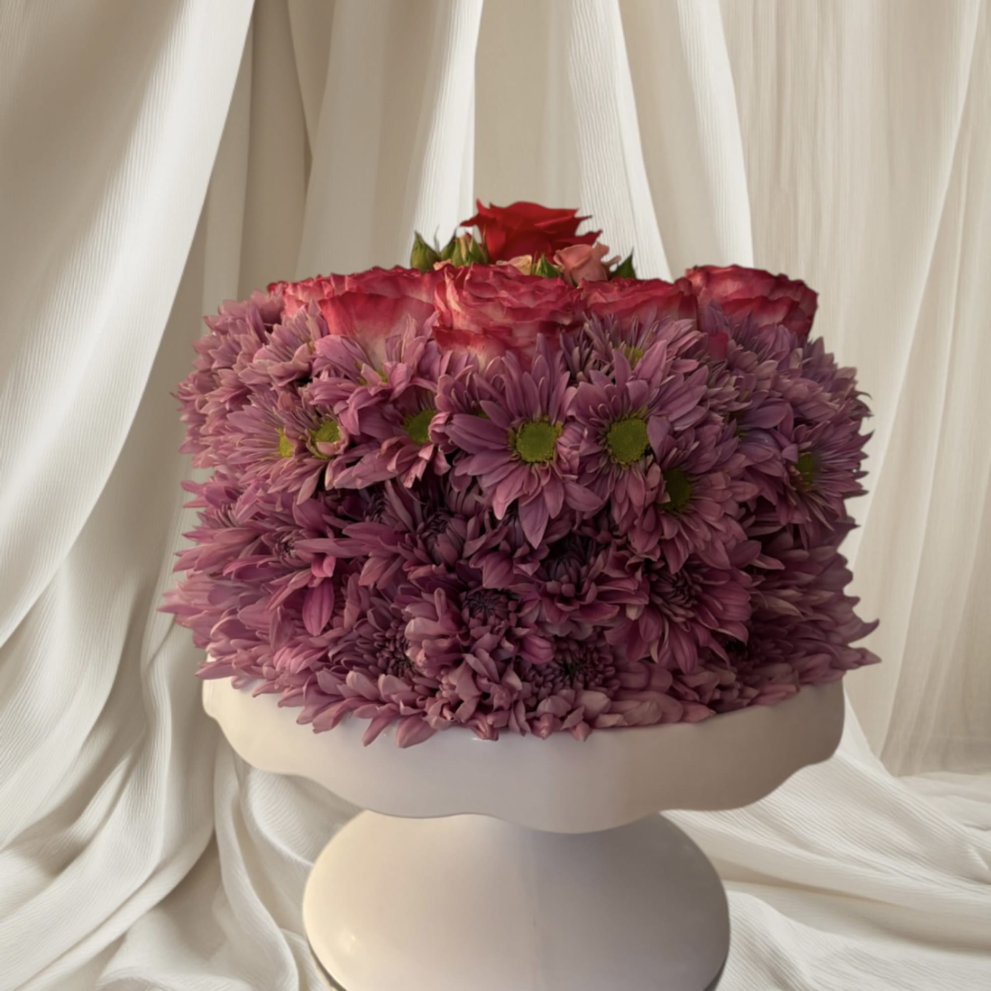 Pink and purple flower arrangement in a white pedestal vase
