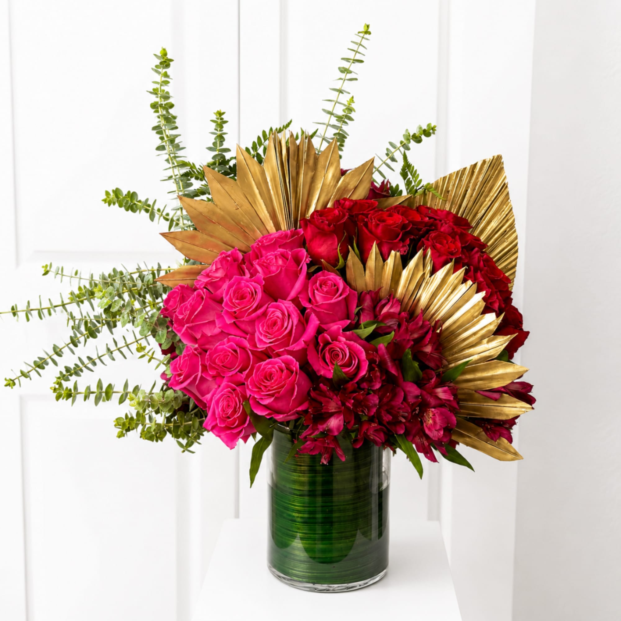 Pink and red roses arranged in a green glass vase with gold leaf accents.