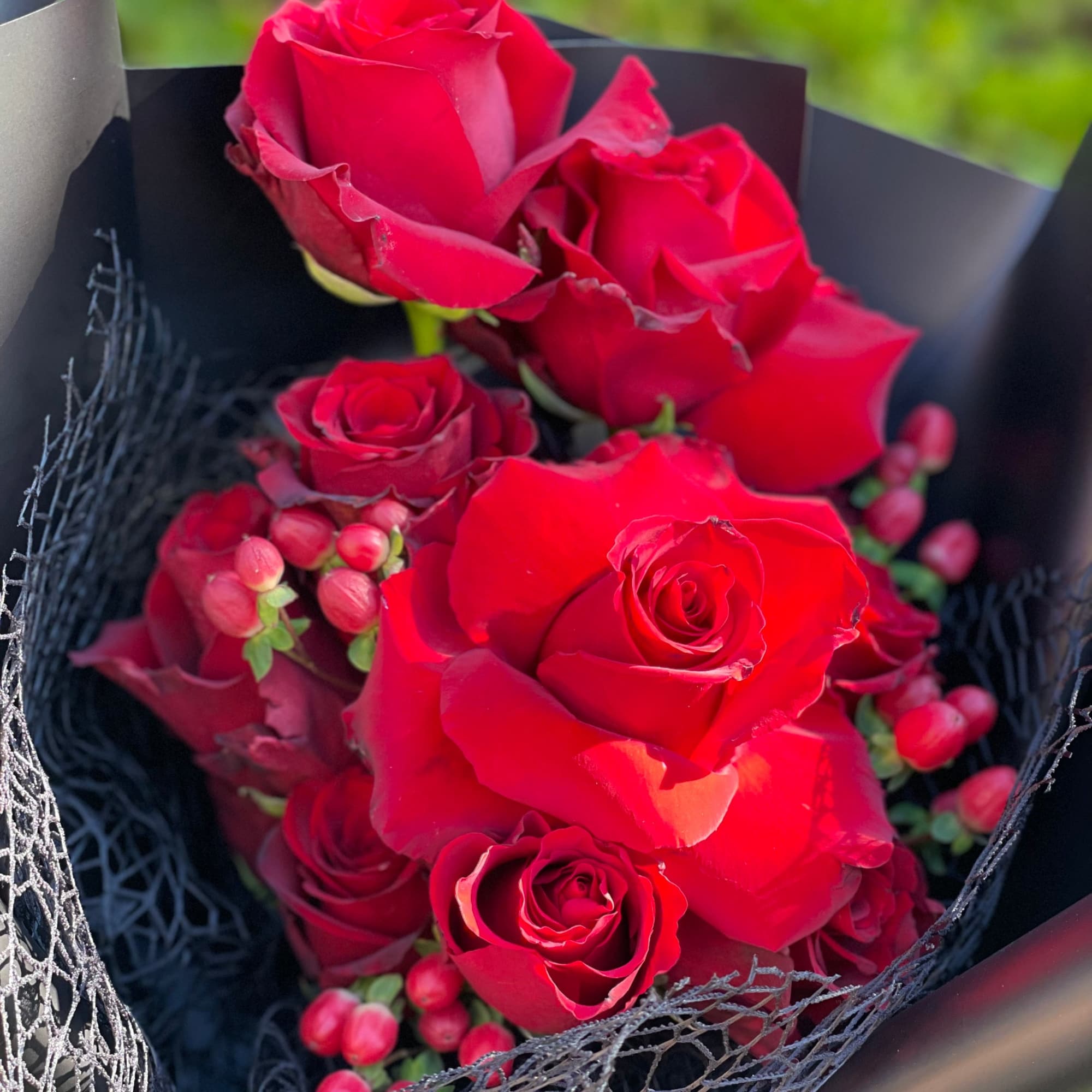 Bouquet of red roses with red berries wrapped in black paper and mesh