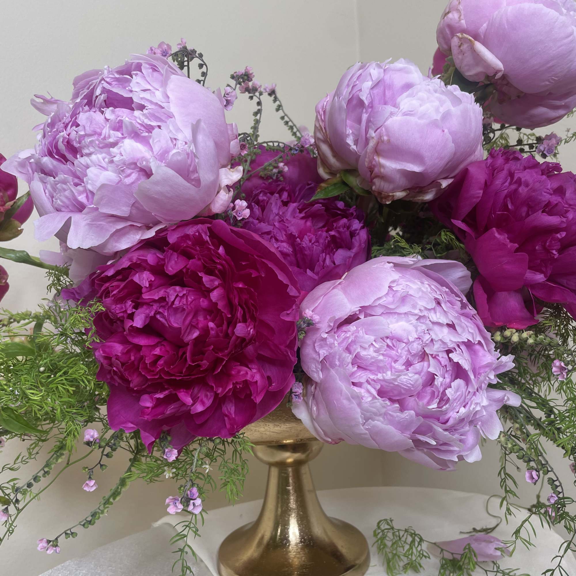 Gold pedestal vase with lush light and dark pink peonies and trailing greenery