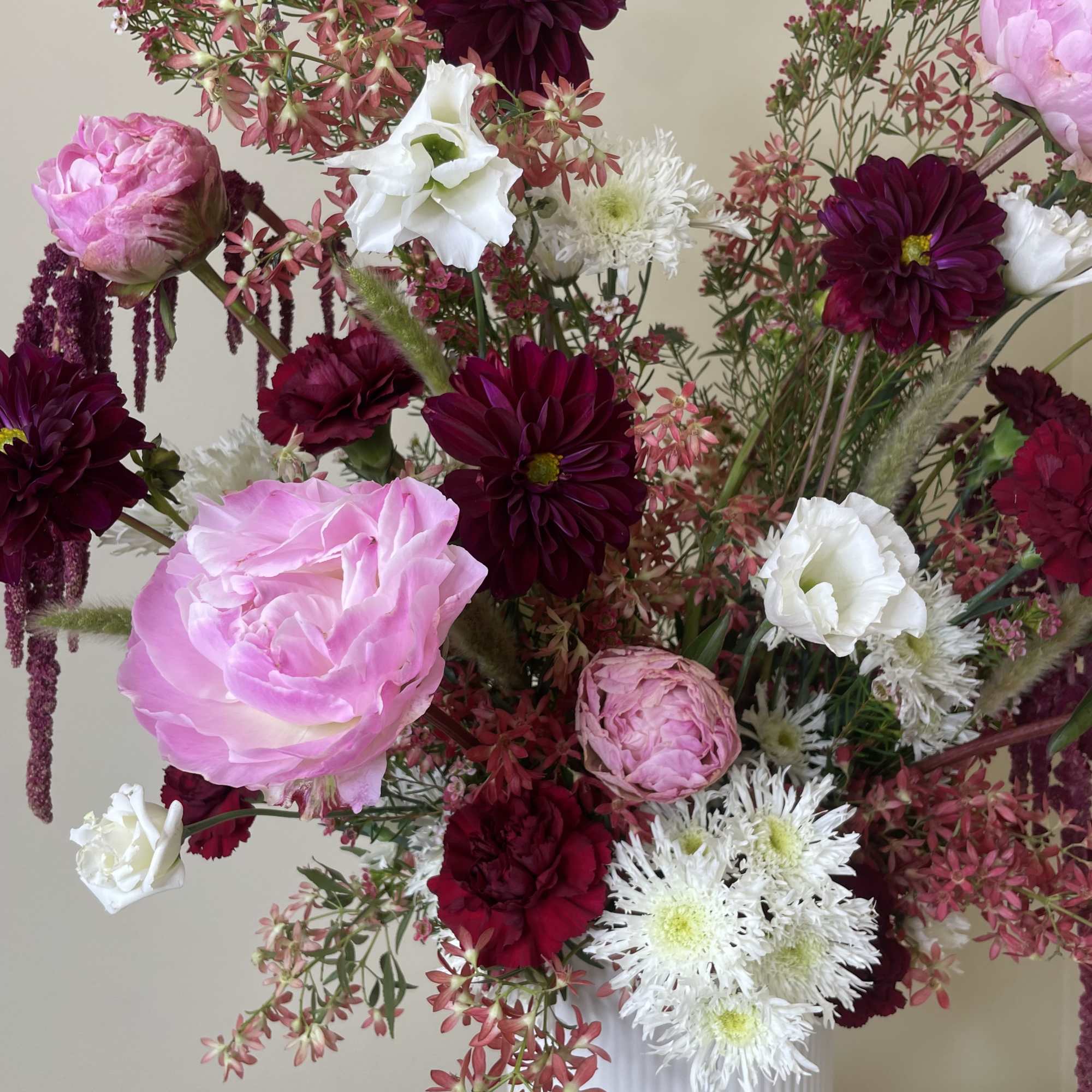 Tall arrangement of pink peonies, burgundy dahlias, and white mums in a white ribbed ceramic vase