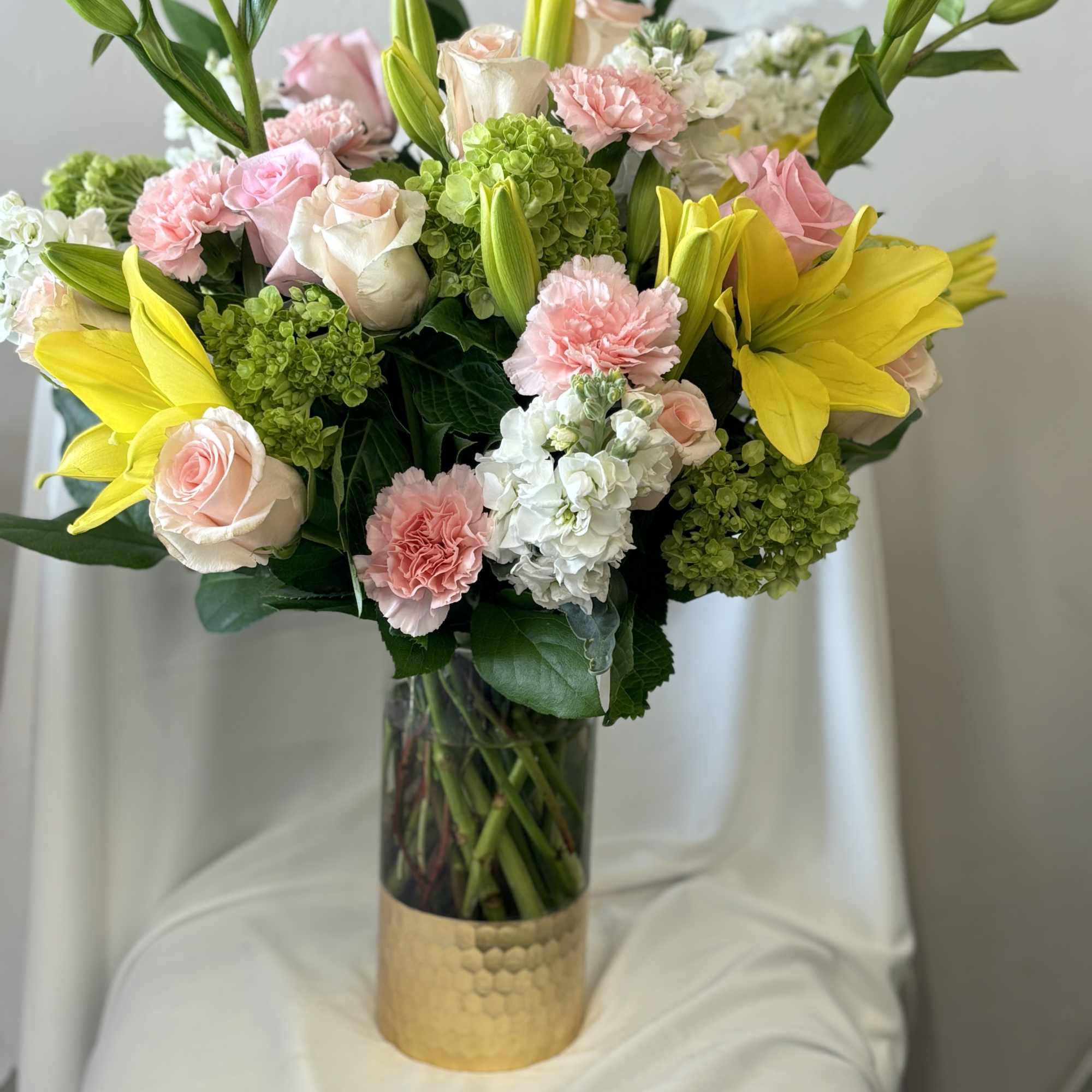 Bouquet of pink roses, yellow lilies, and green hydrangeas in a glass vase