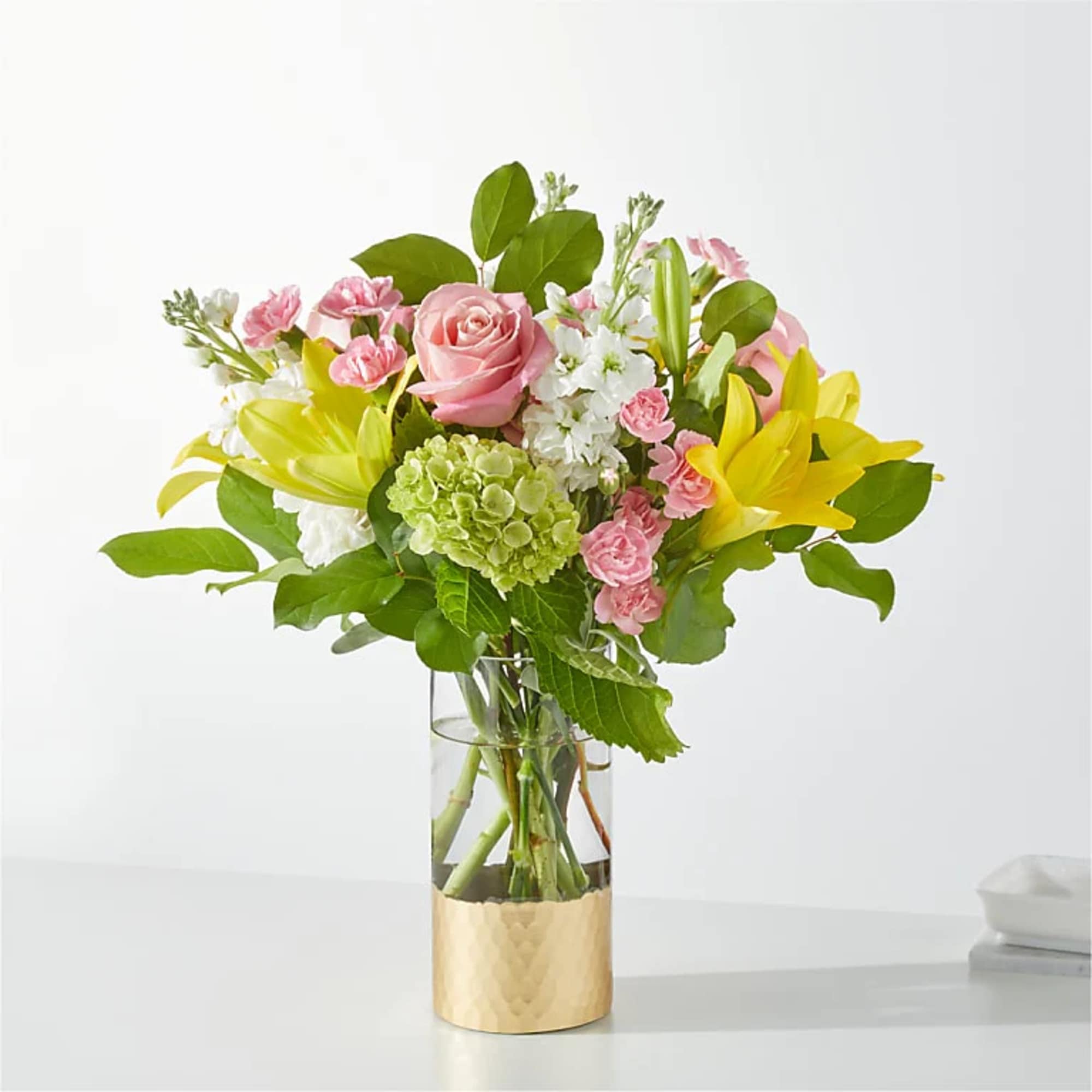 Pink roses and yellow lilies in a clear glass vase with a gold base