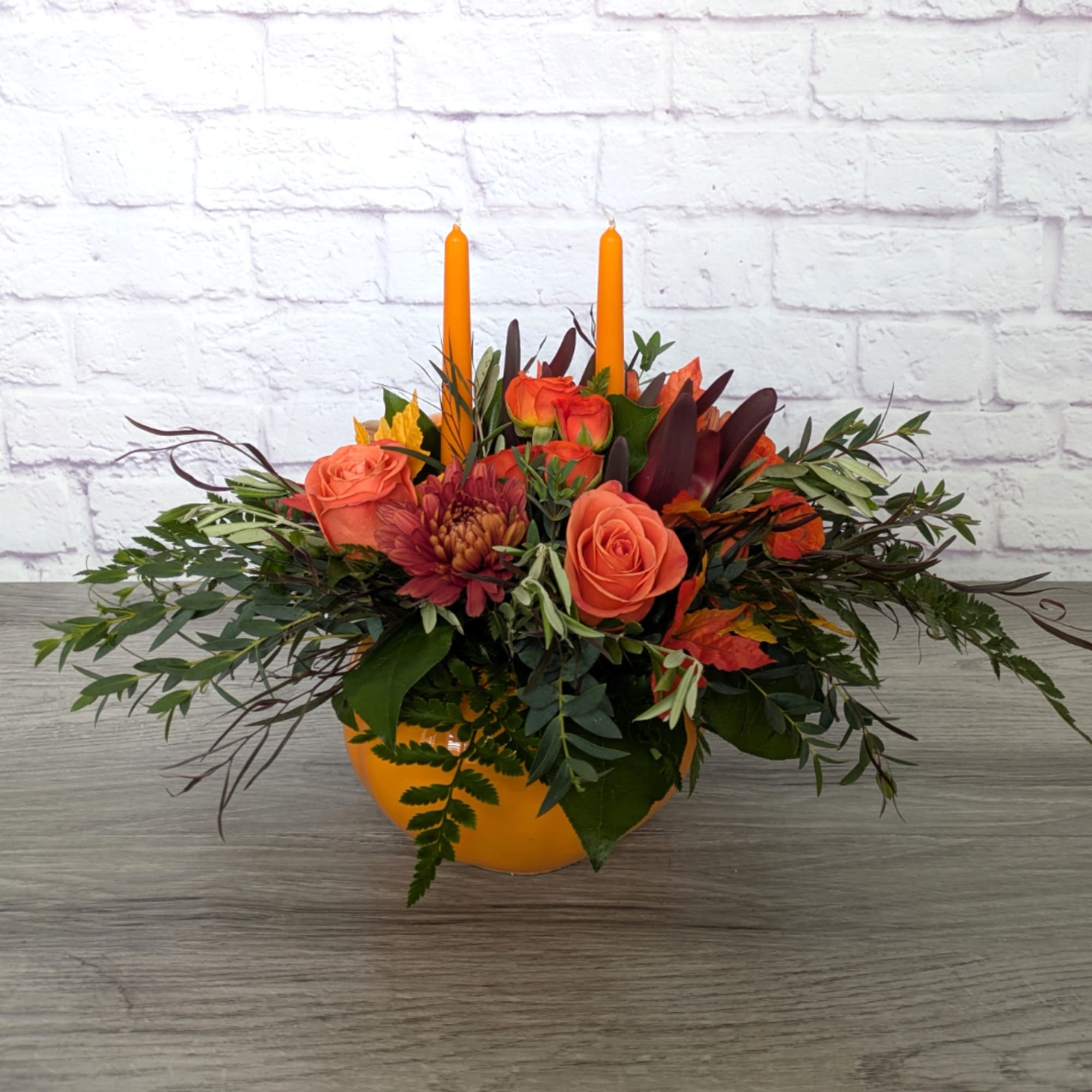 Orange rose arrangement in a round orange vase with two taper candles
