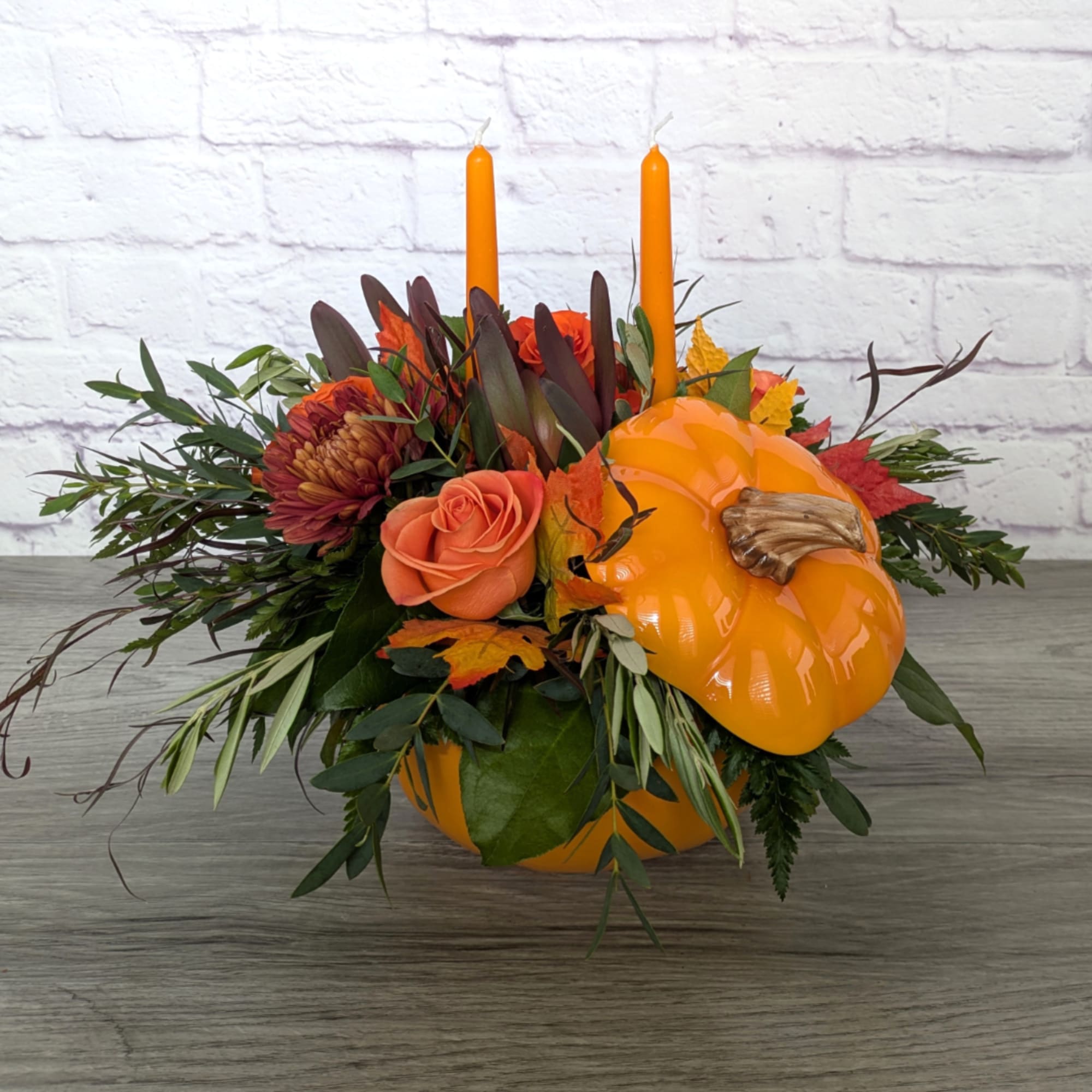 Orange pumpkin centerpiece with roses, mums, and two taper candles