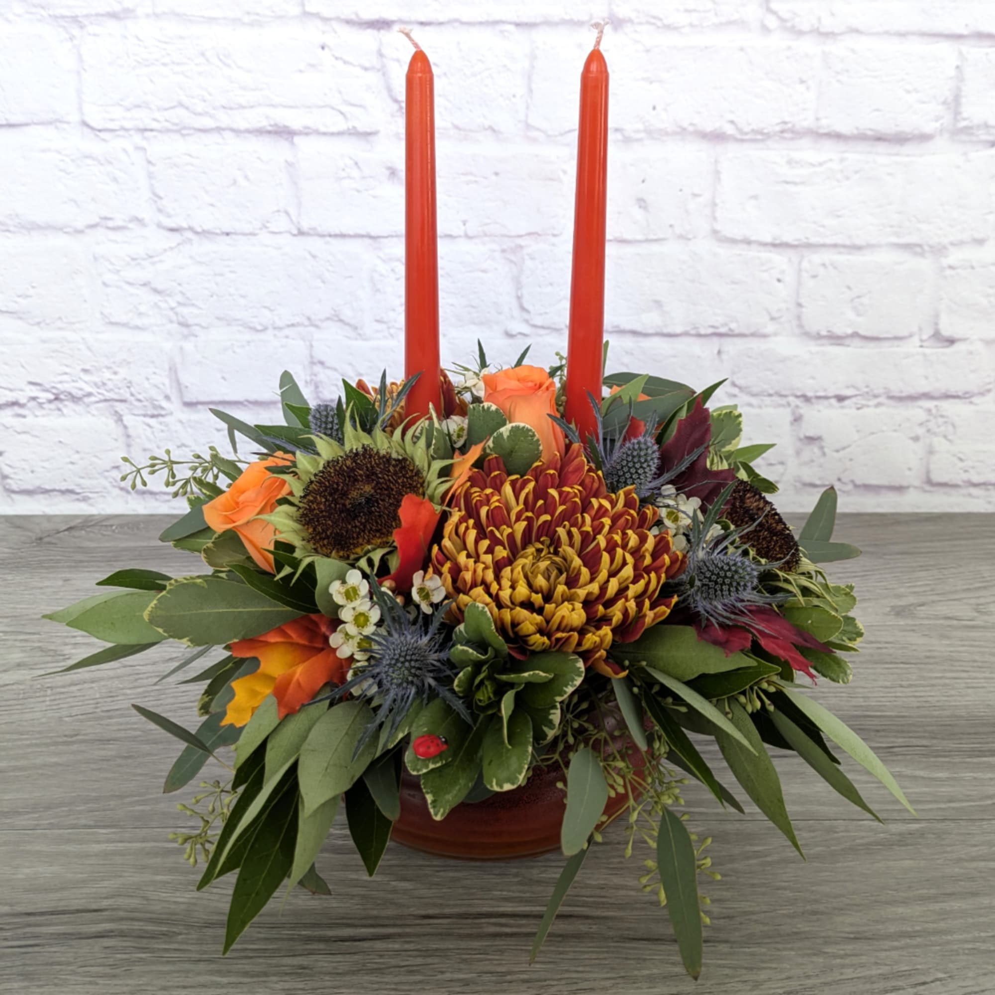 Orange and burgundy floral centerpiece with two tall red candles