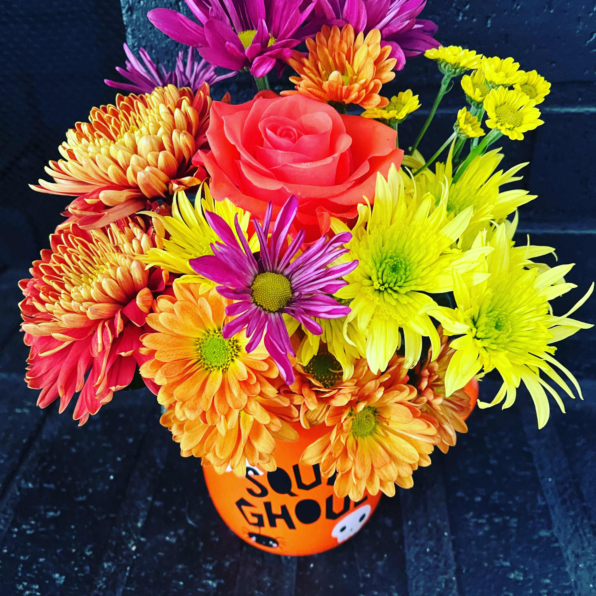 Bright mixed bouquet in an orange Halloween bucket with a pink rose
