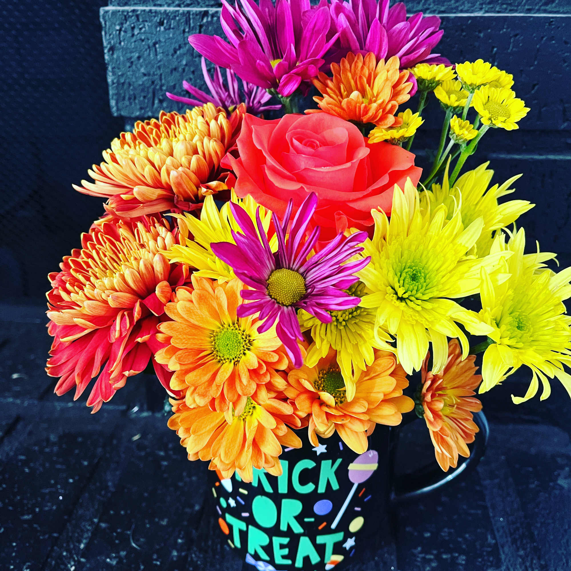 Colorful bouquet of daisies and a rose in a Halloween mug