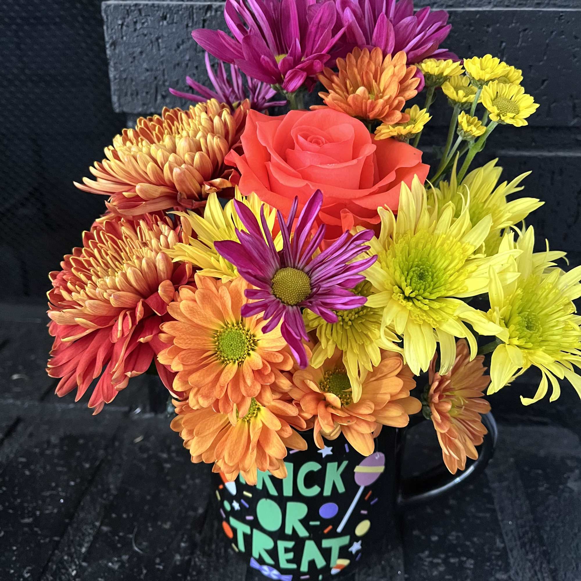 Bright mixed bouquet in a black mug with a red rose and colorful daisies