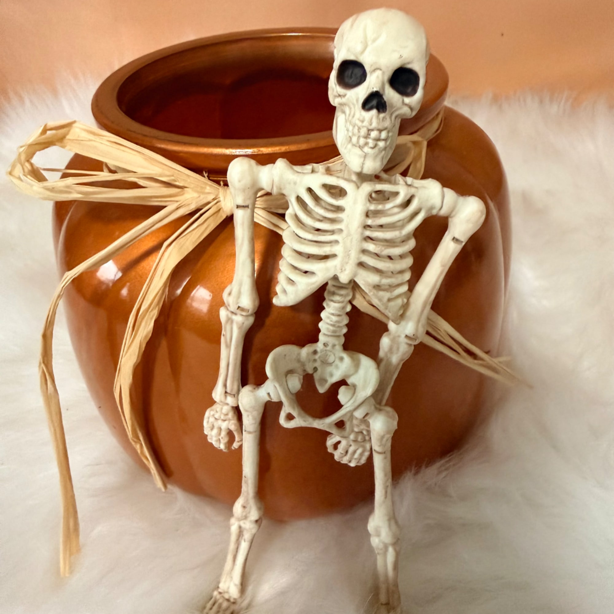 Small orange vase with a decorative skeleton and raffia bow