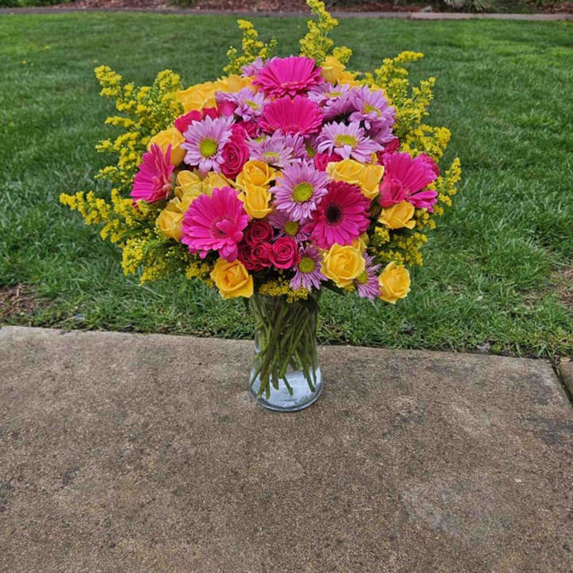 Bright mixed bouquet in a clear glass vase on a sidewalk