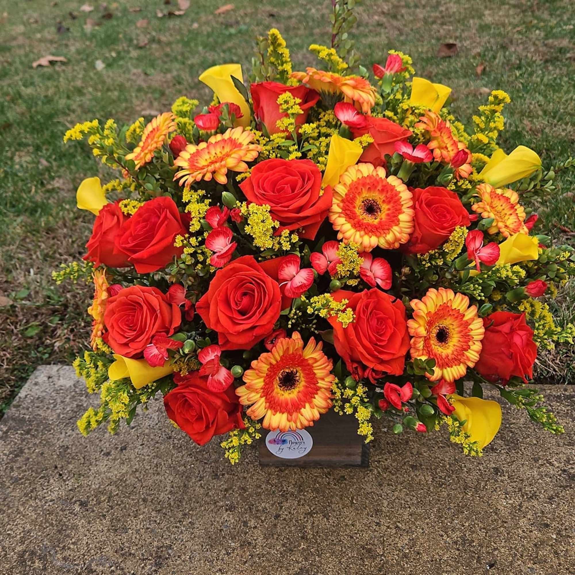 Bright bouquet of red roses, orange gerberas, and yellow calla lilies in a wooden box