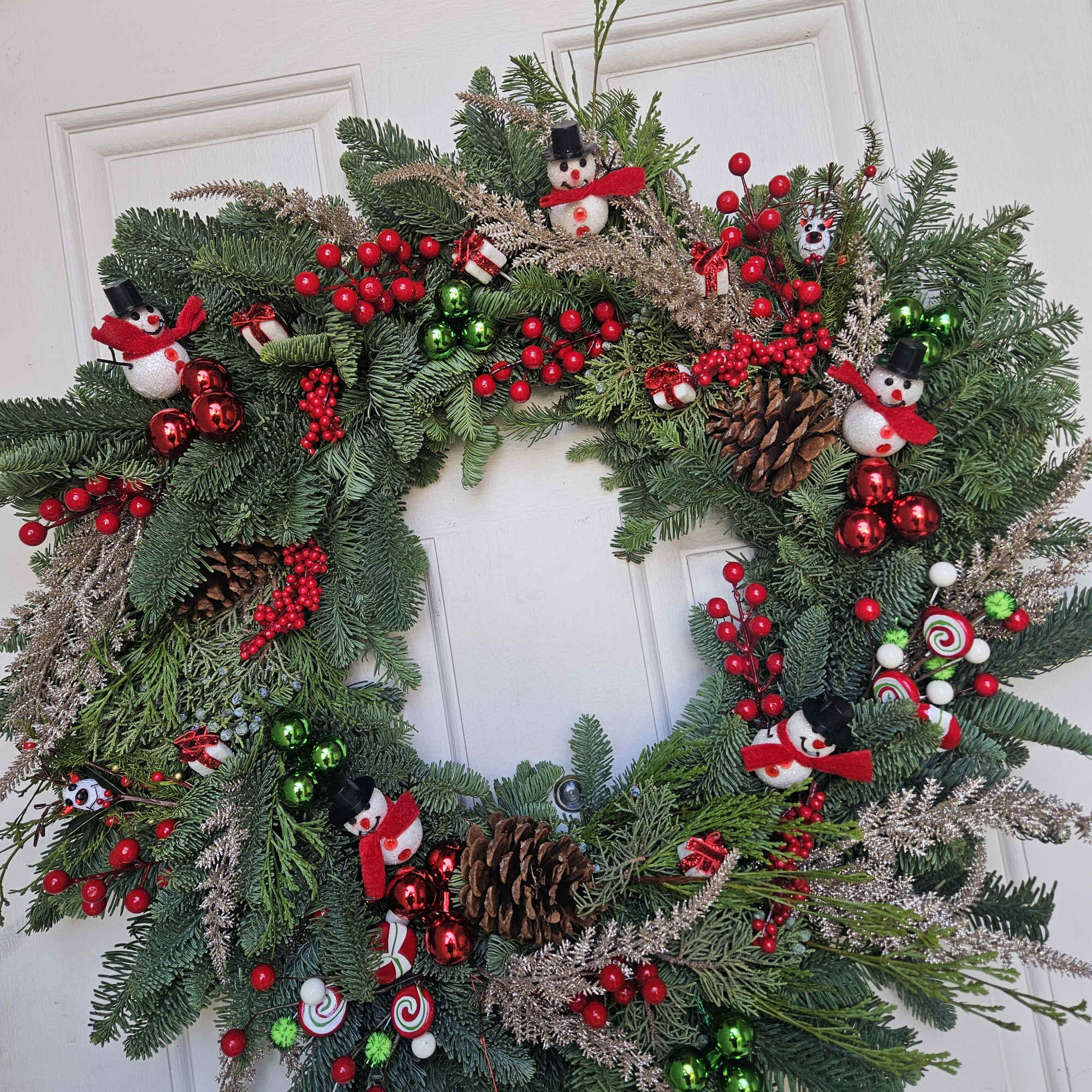 Christmas wreath with pine branches, red berries, pinecones, and snowman ornaments