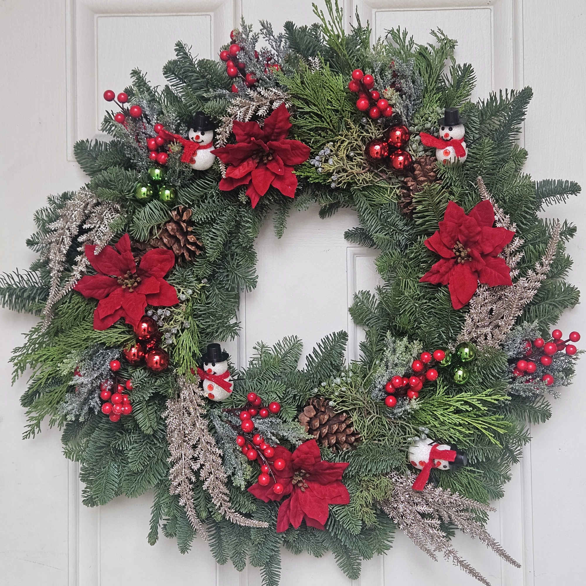 Christmas wreath with red poinsettias, berries, pinecones, and snowman ornaments