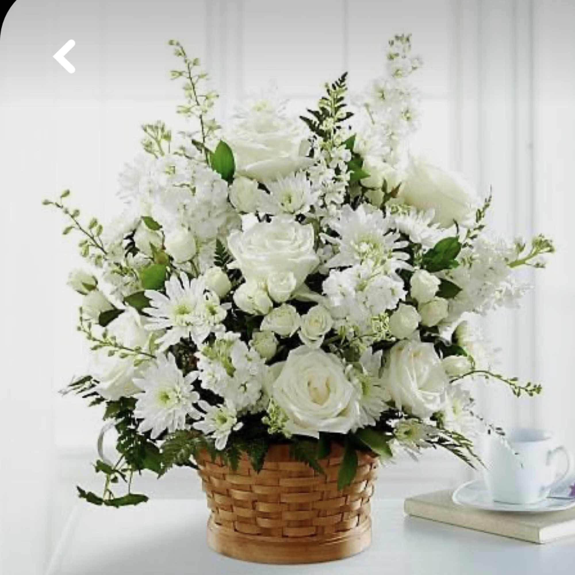 White floral arrangement in a woven basket with a cup and book nearby