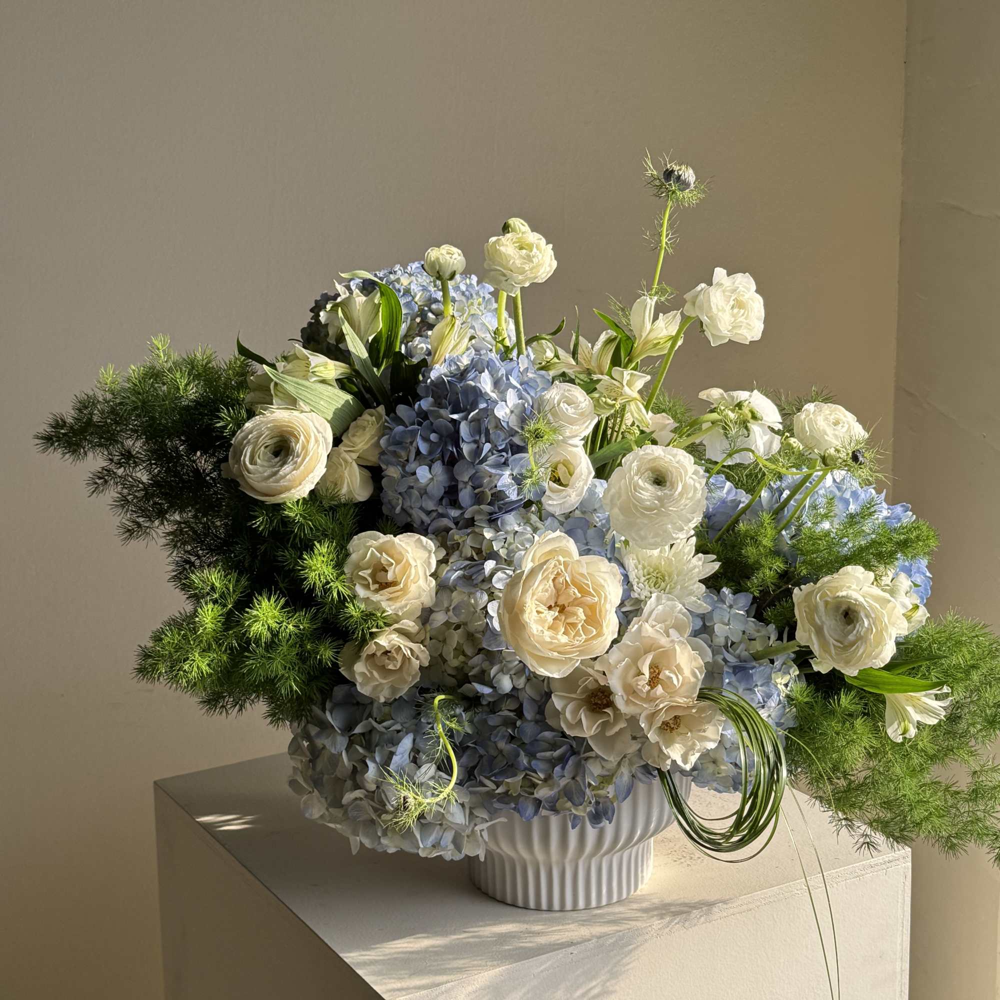 Blue hydrangea and white rose arrangement in a white vase