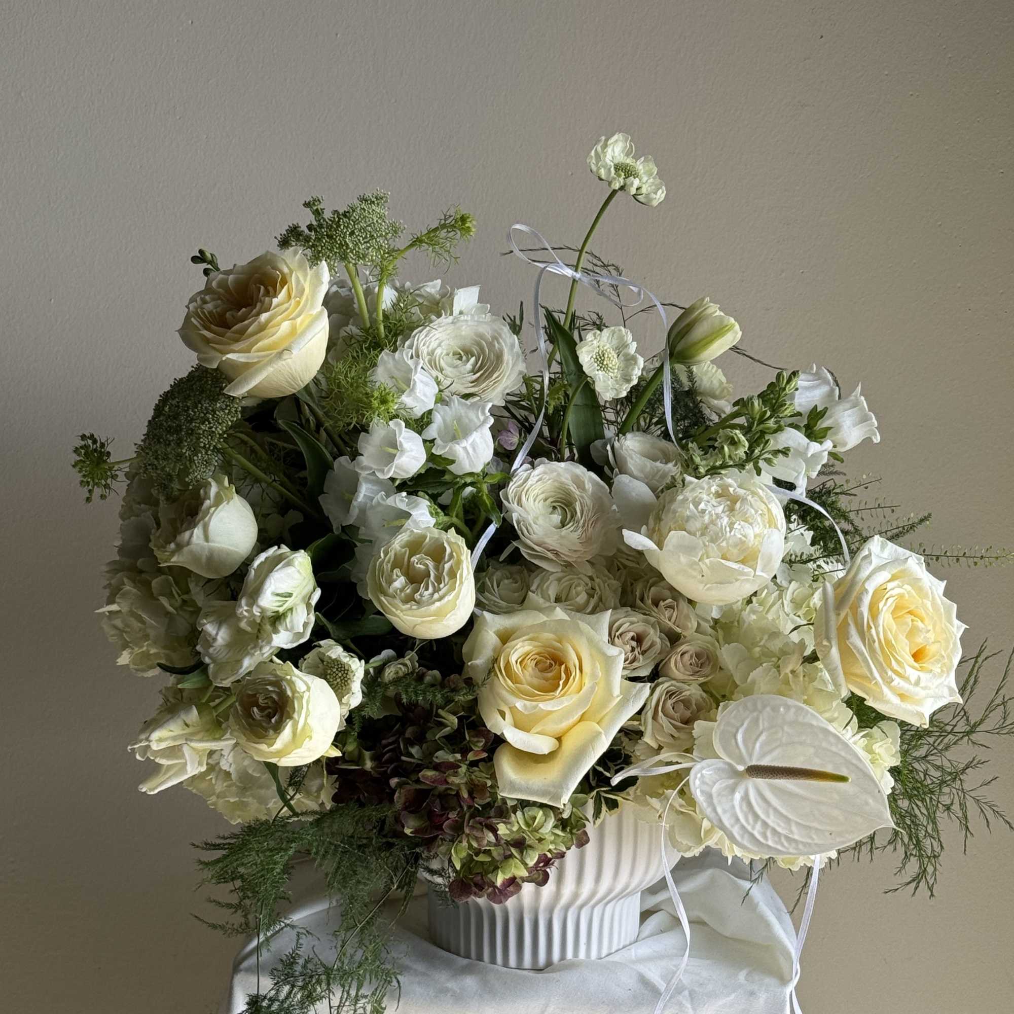 Cream and white floral arrangement in a ribbed white vase with ribbon accents
