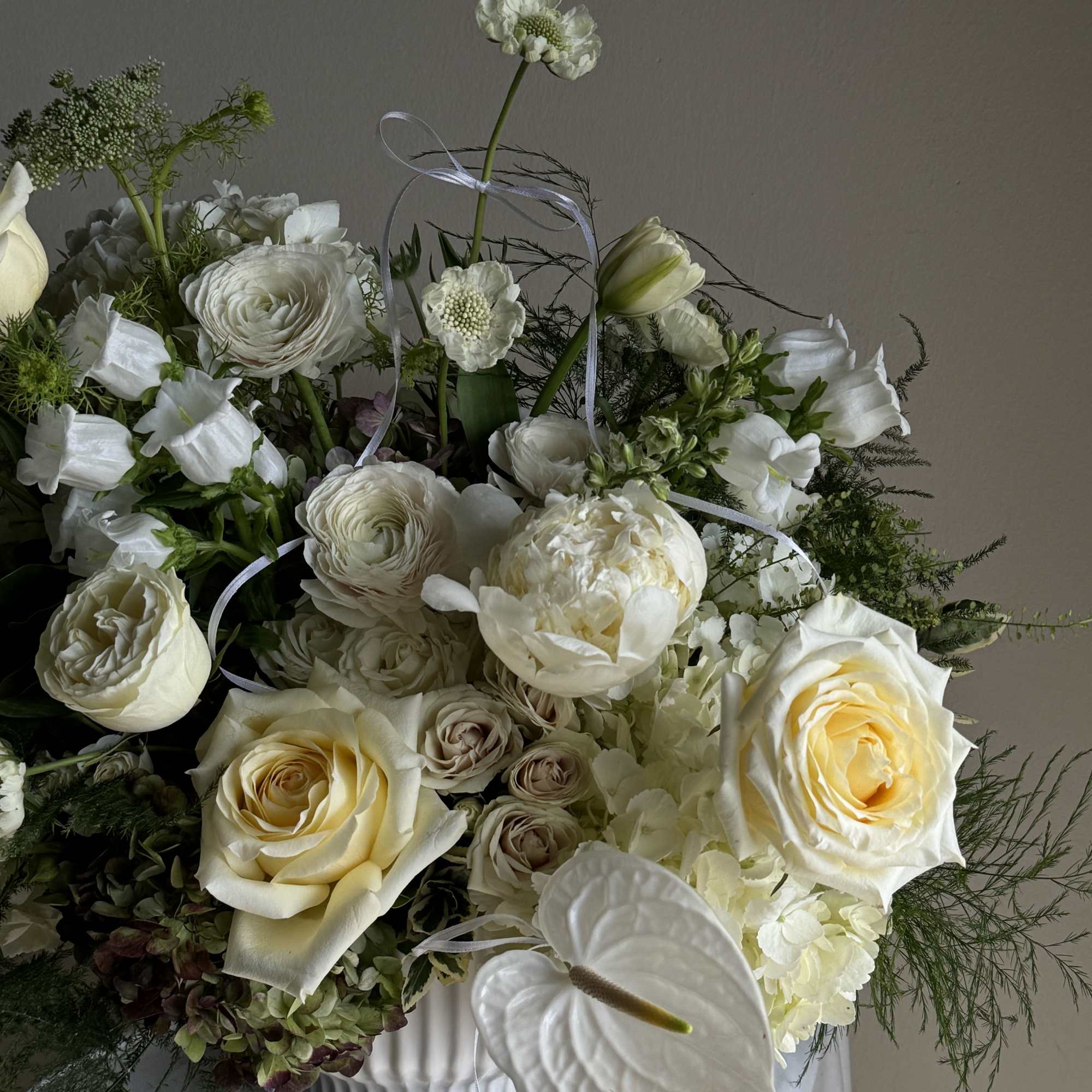 White and cream floral arrangement with roses and anthurium in a white vase