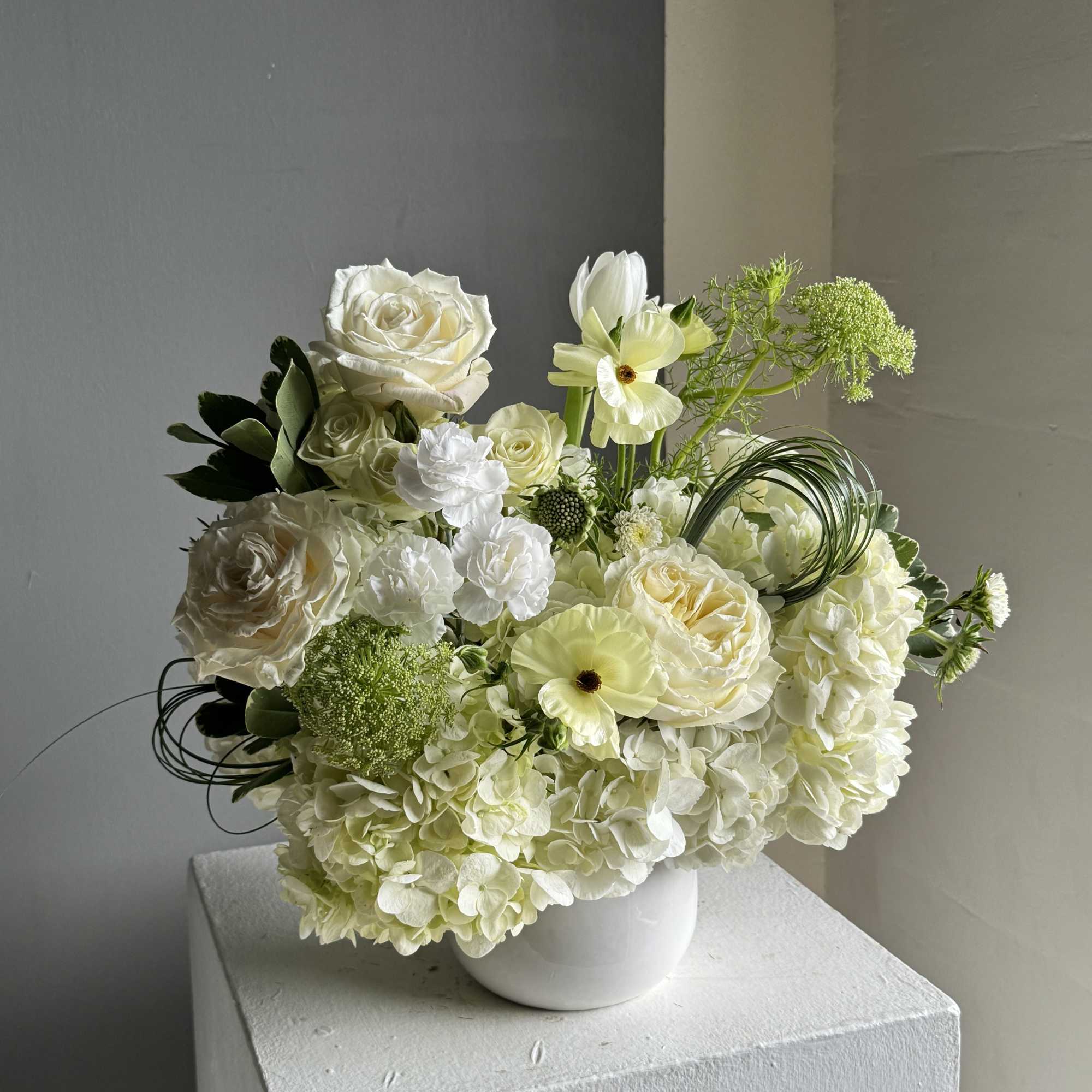 White floral arrangement in a white vase with roses and hydrangeas