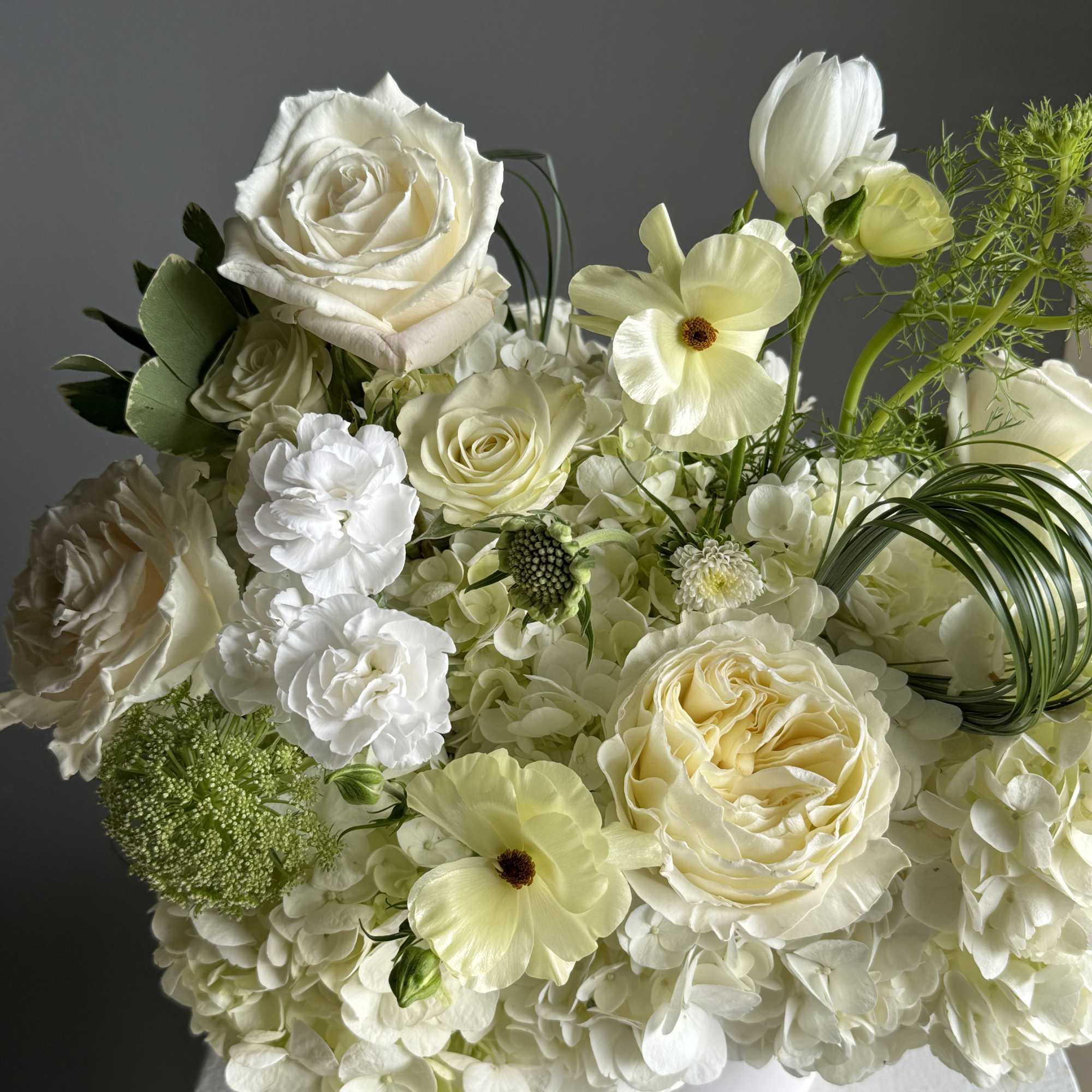 White floral arrangement with roses, hydrangea, and pale yellow blooms in a vase