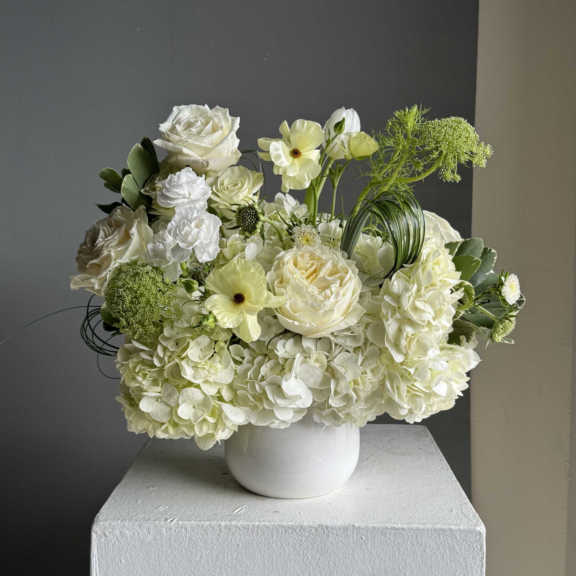 White floral arrangement in a white vase with roses and hydrangeas