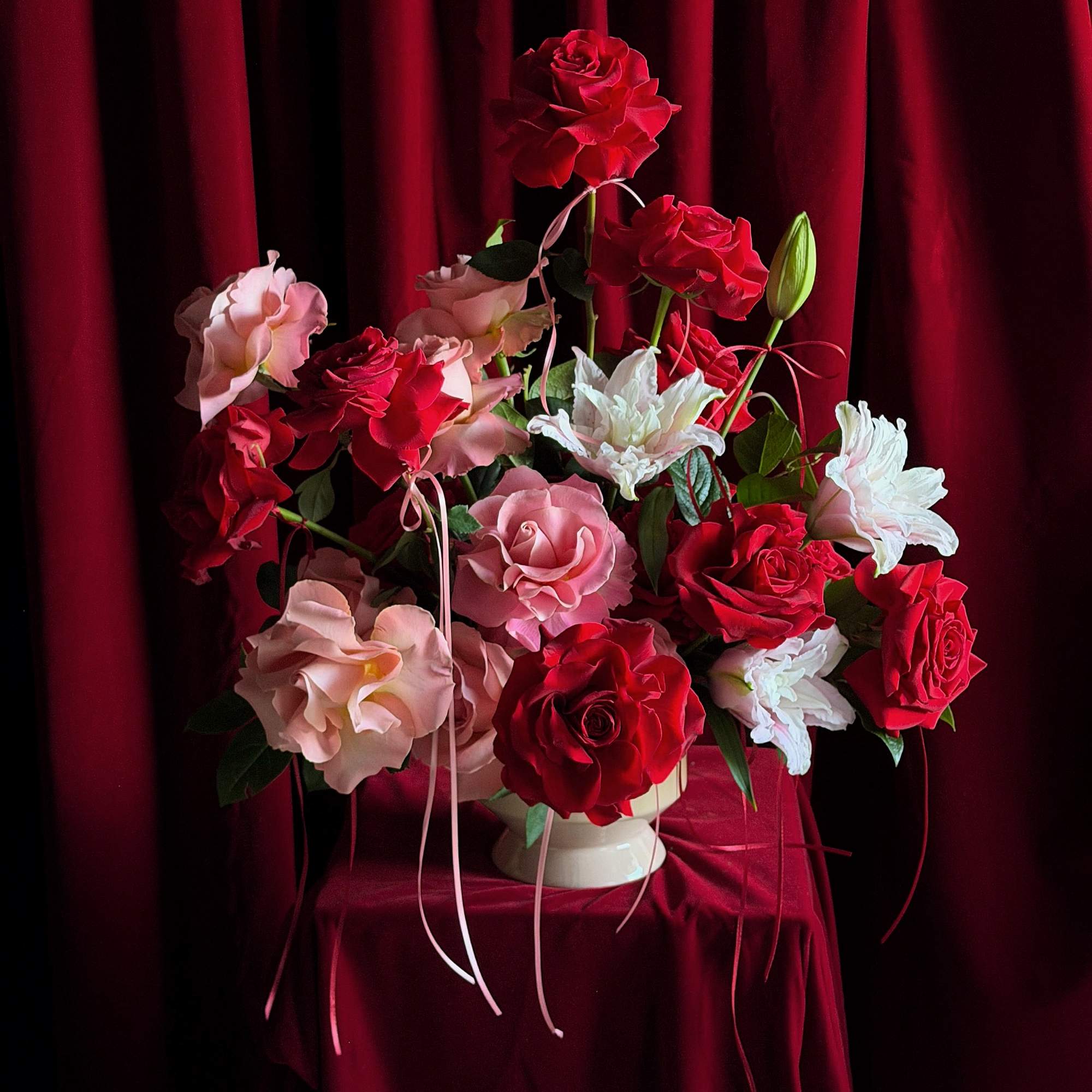 Red and pink roses arranged in a white vase against a burgundy backdrop
