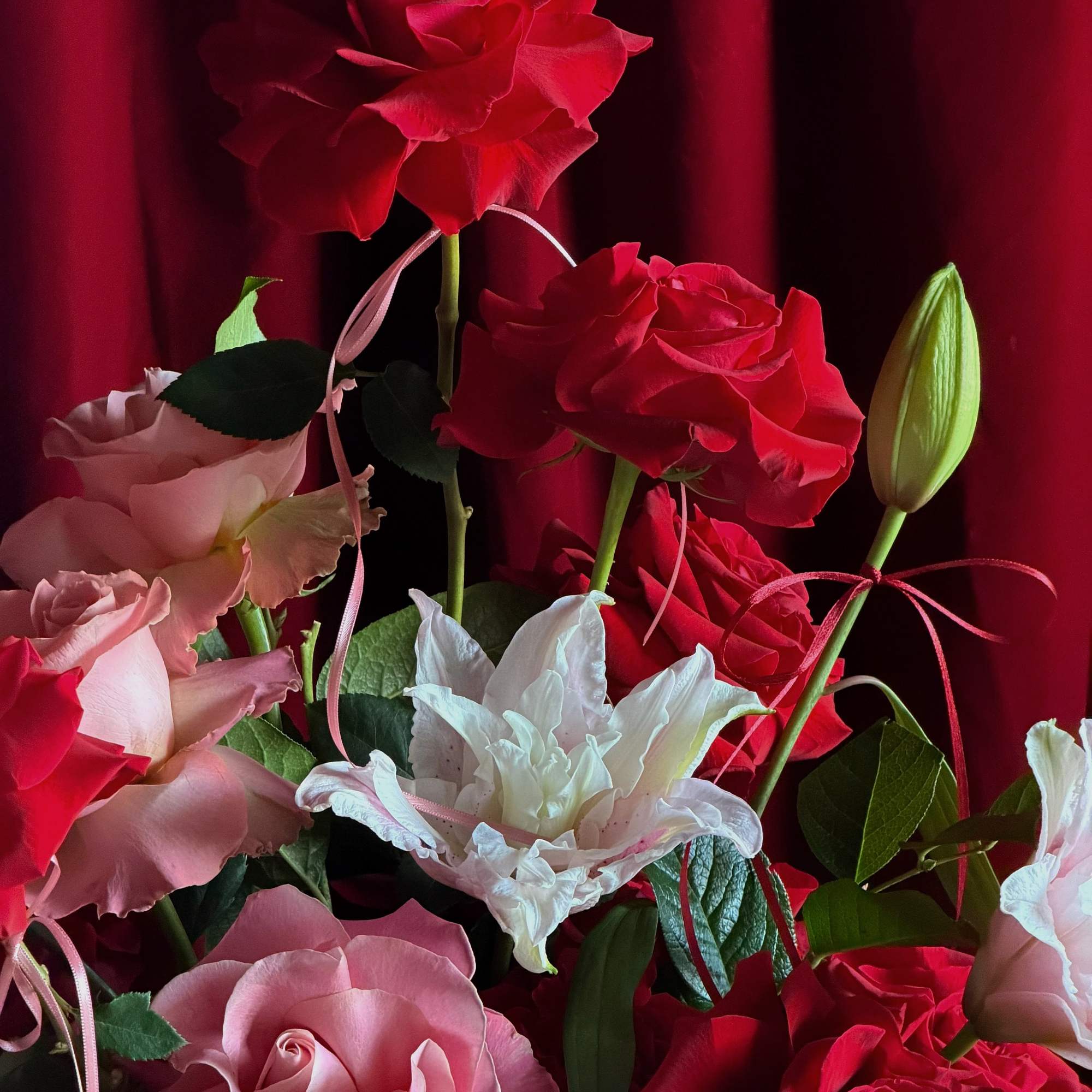 Bouquet of red, pink, and white roses with a lily bud
