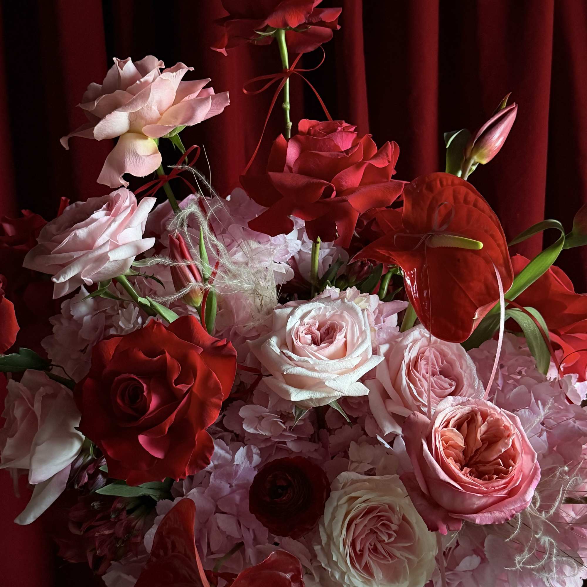 Red and pink roses with red anthuriums in a white vase