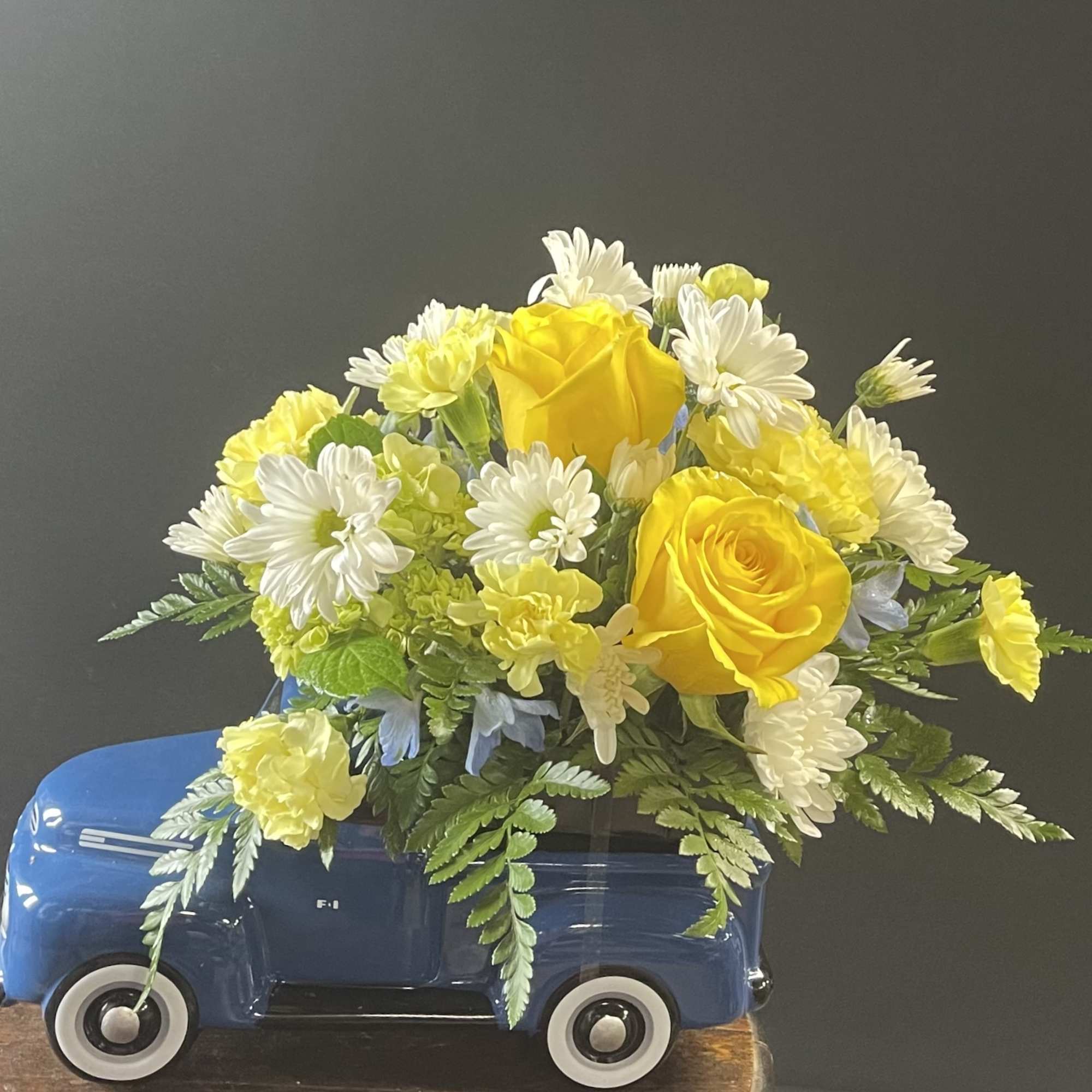 Yellow roses and white daisies arranged in a blue toy truck