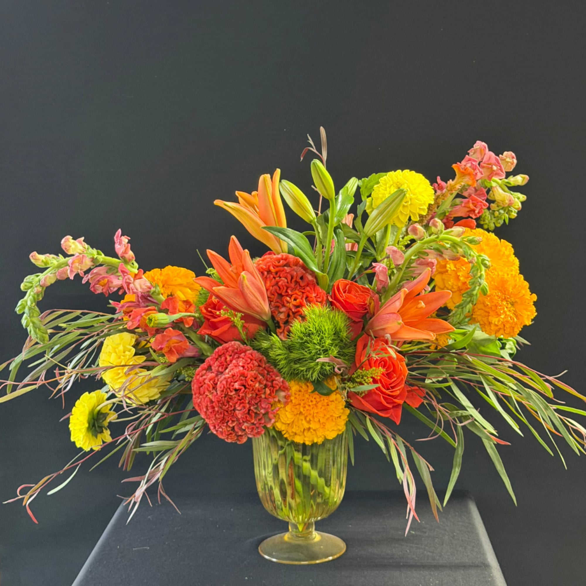 Bright mixed flower arrangement in a glass vase with orange lilies and yellow blooms