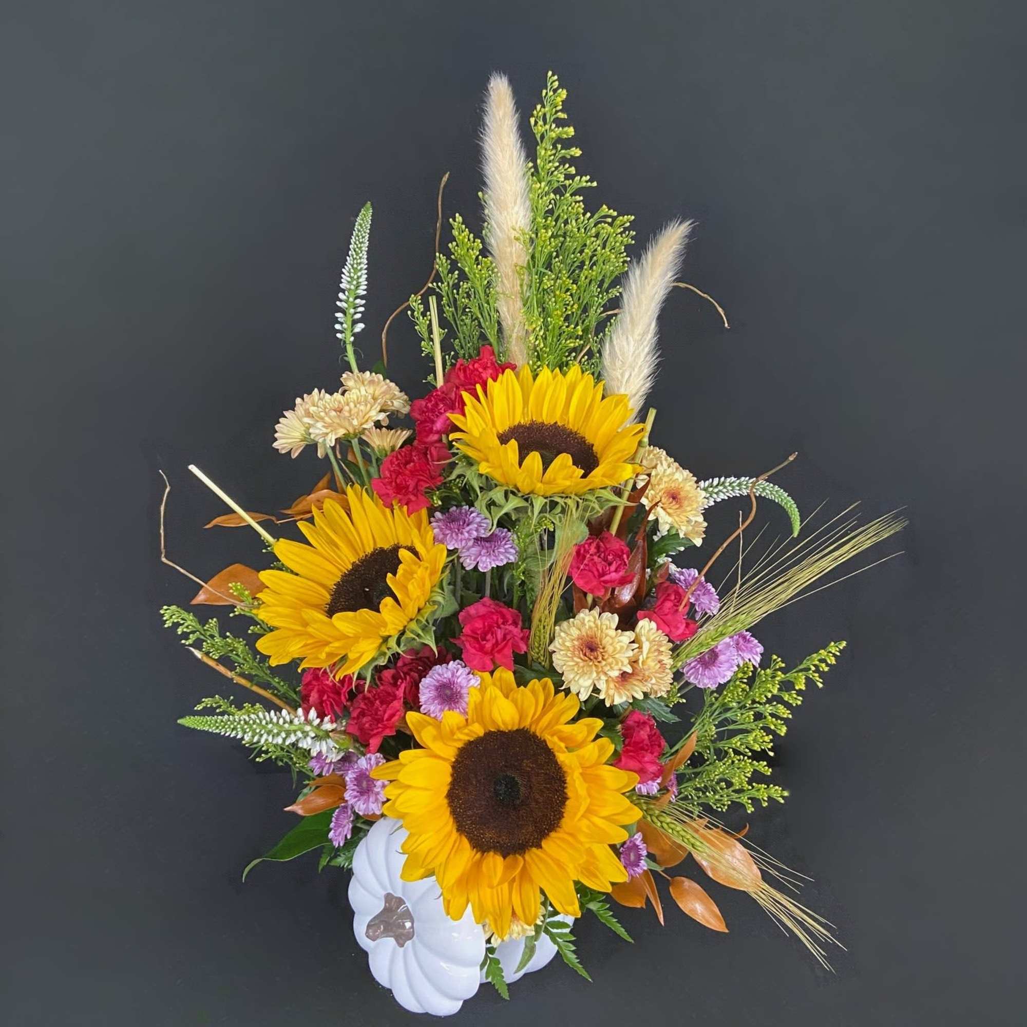 Sunflower arrangement with pink and lavender flowers in a white pumpkin container