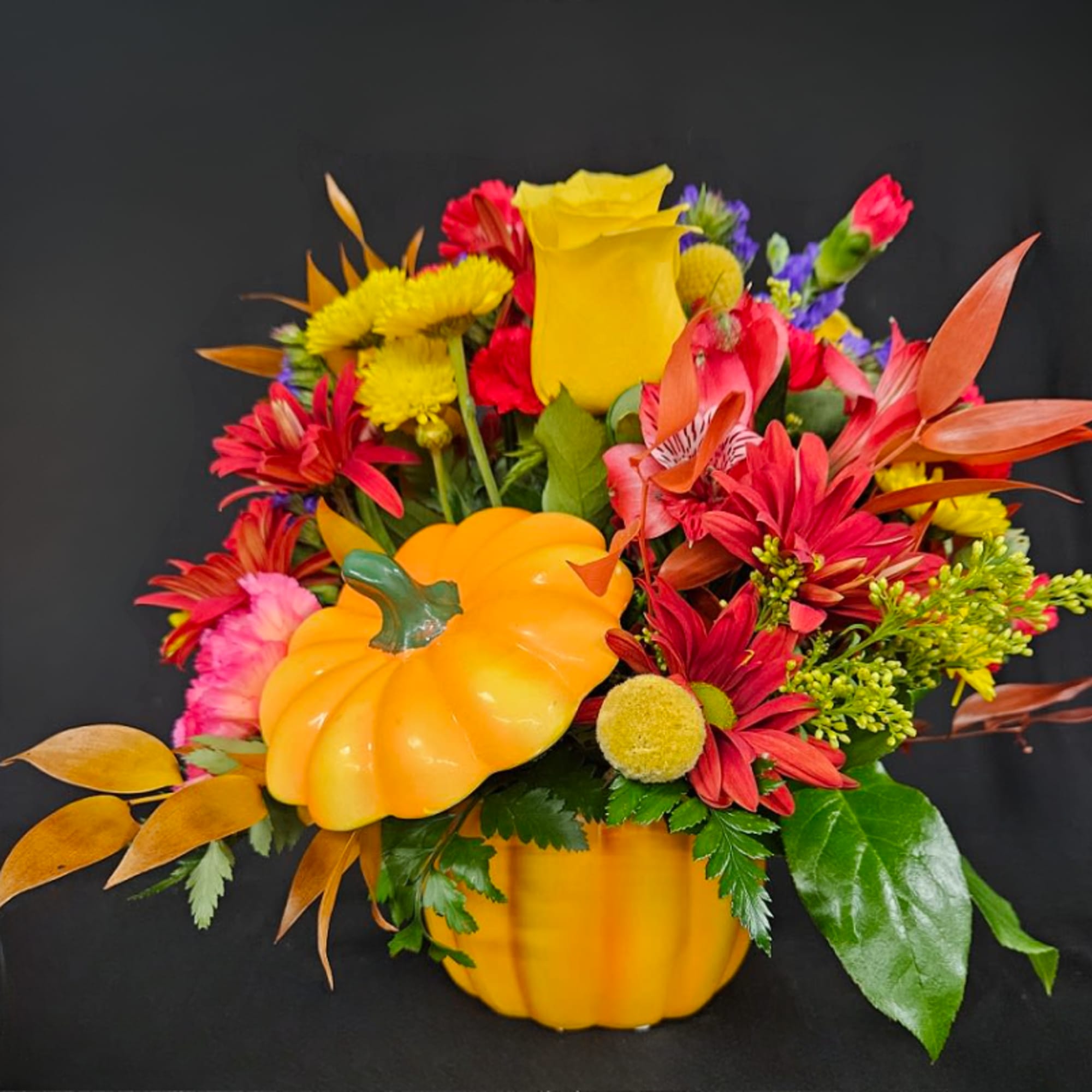 Colorful fall bouquet in a pumpkin-shaped container with red, yellow, and orange flowers