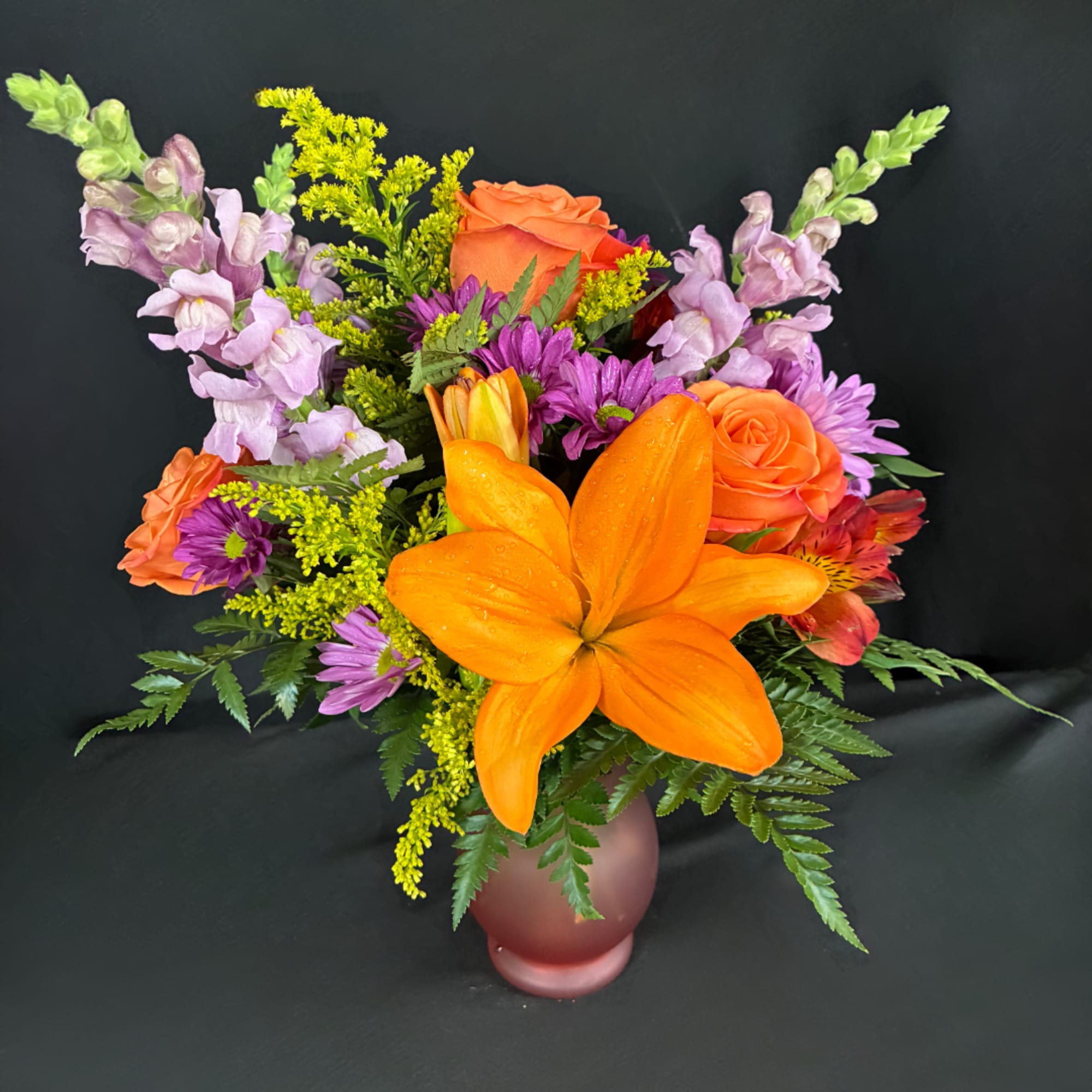 Colorful bouquet with orange lilies, roses, and purple flowers in a frosted vase