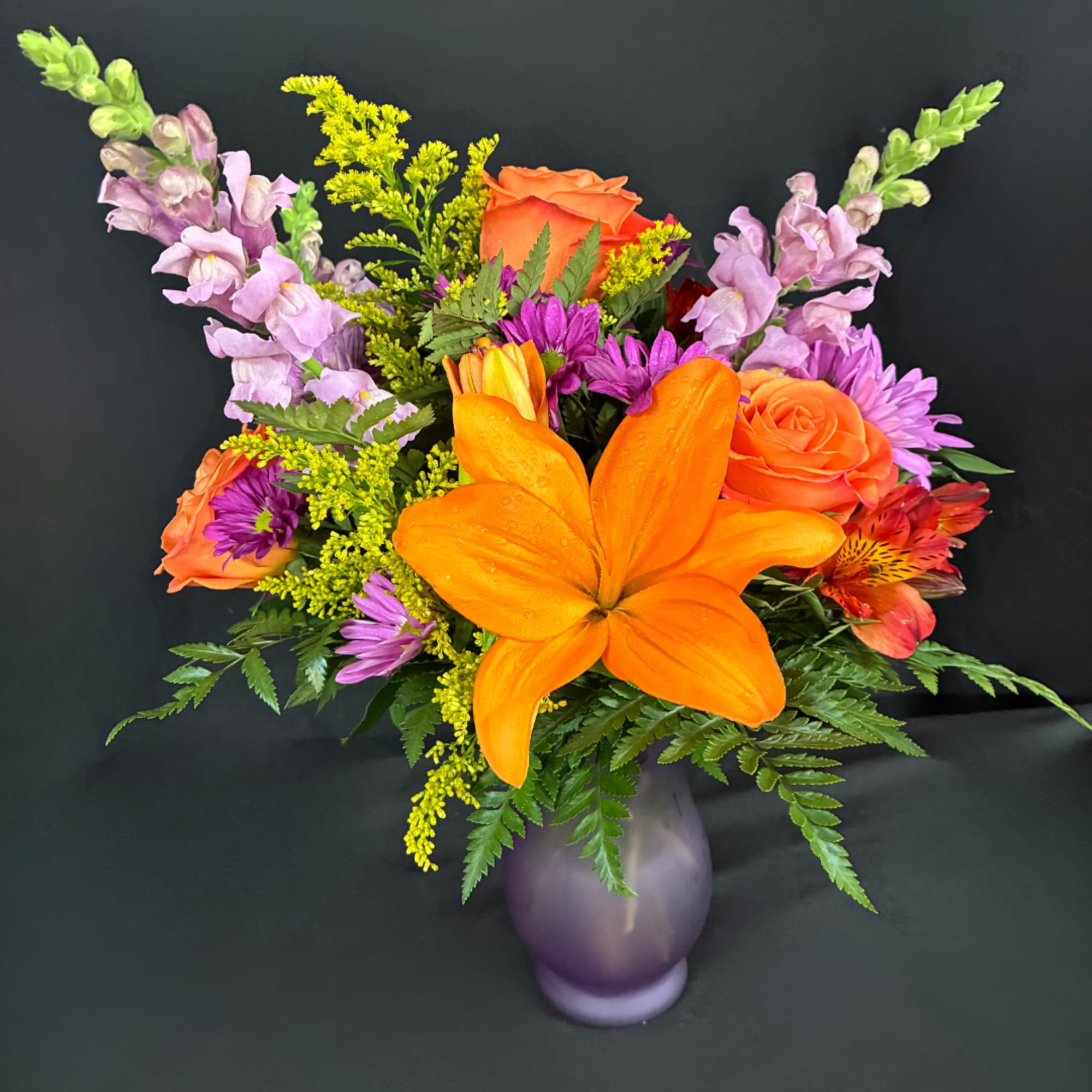 Orange lilies and mixed flowers in a purple vase