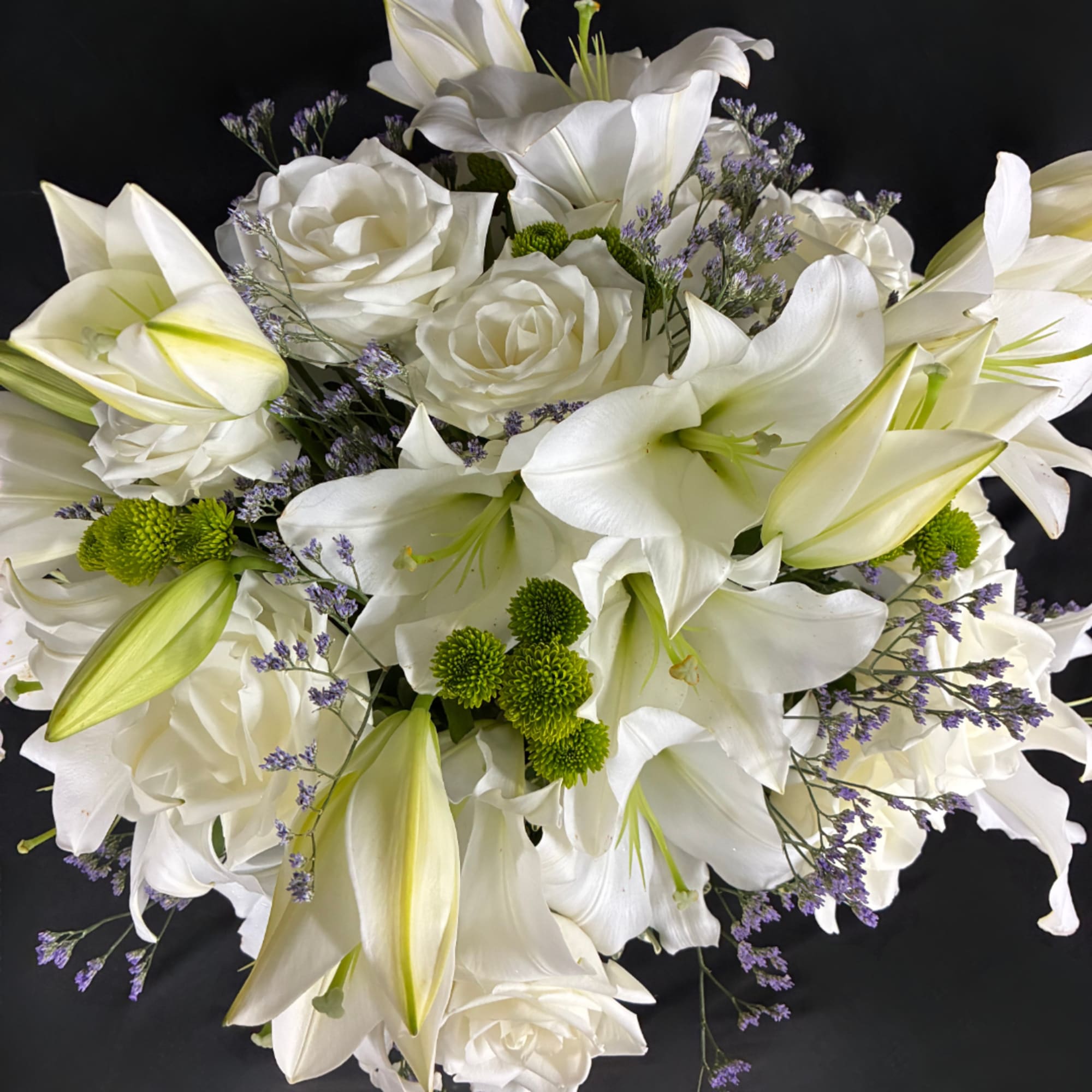 White lilies and roses arranged with small purple filler flowers