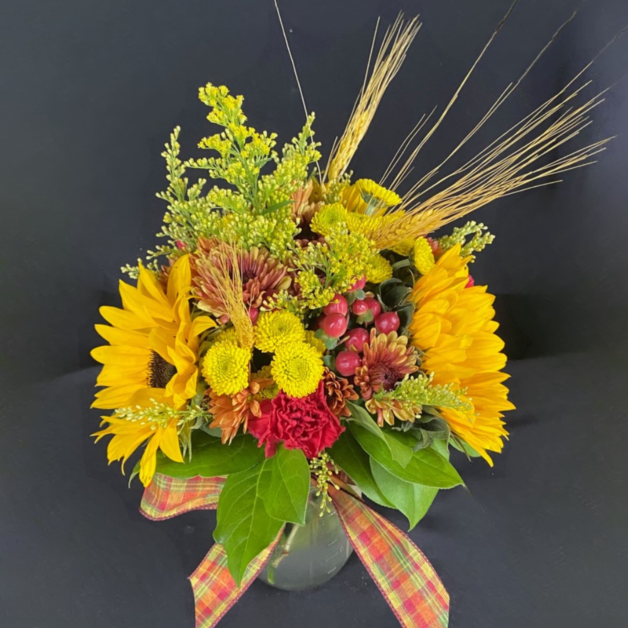 Sunflower and chrysanthemum arrangement in a glass vase with plaid ribbon
