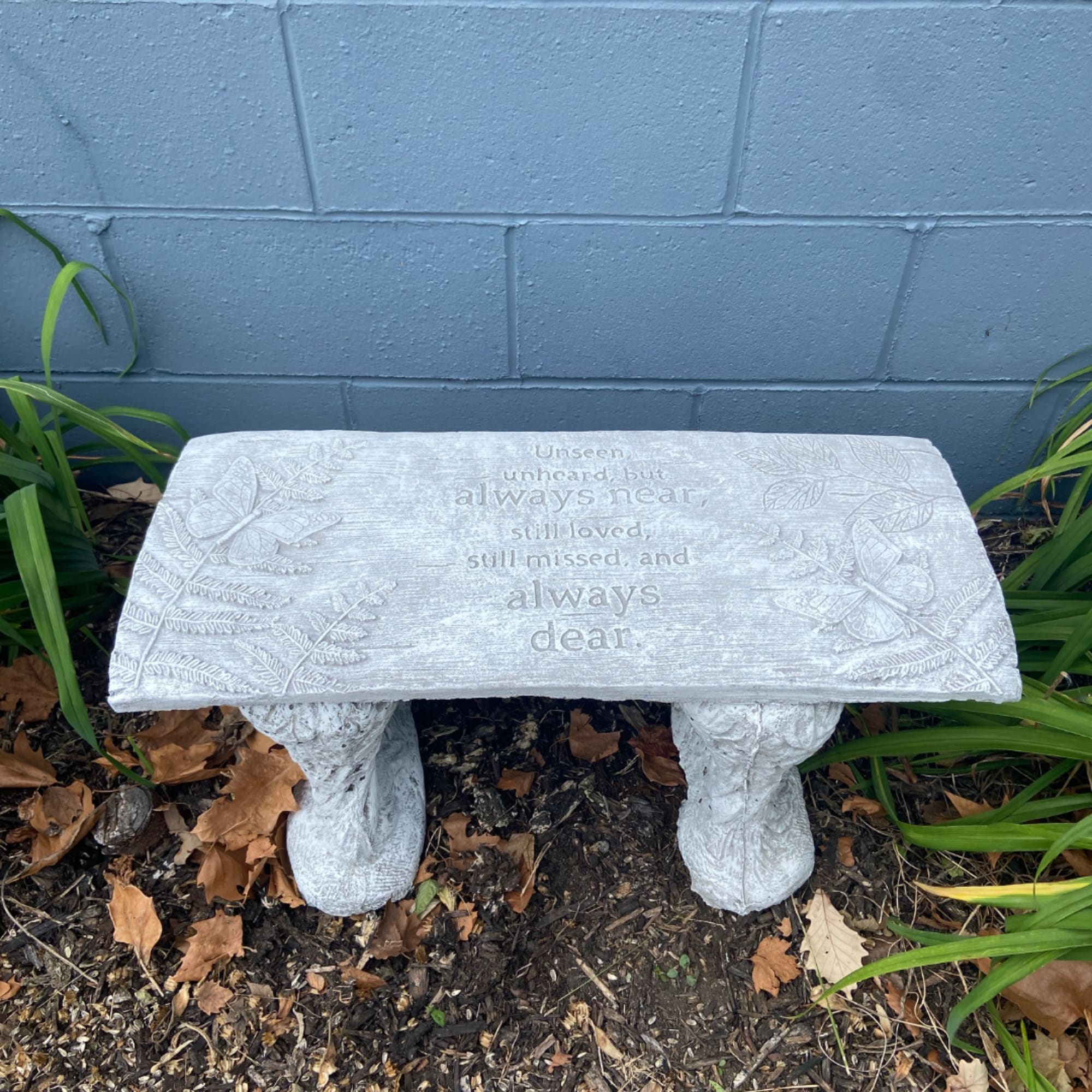 White memorial bench with engraved text and floral reliefs outdoors