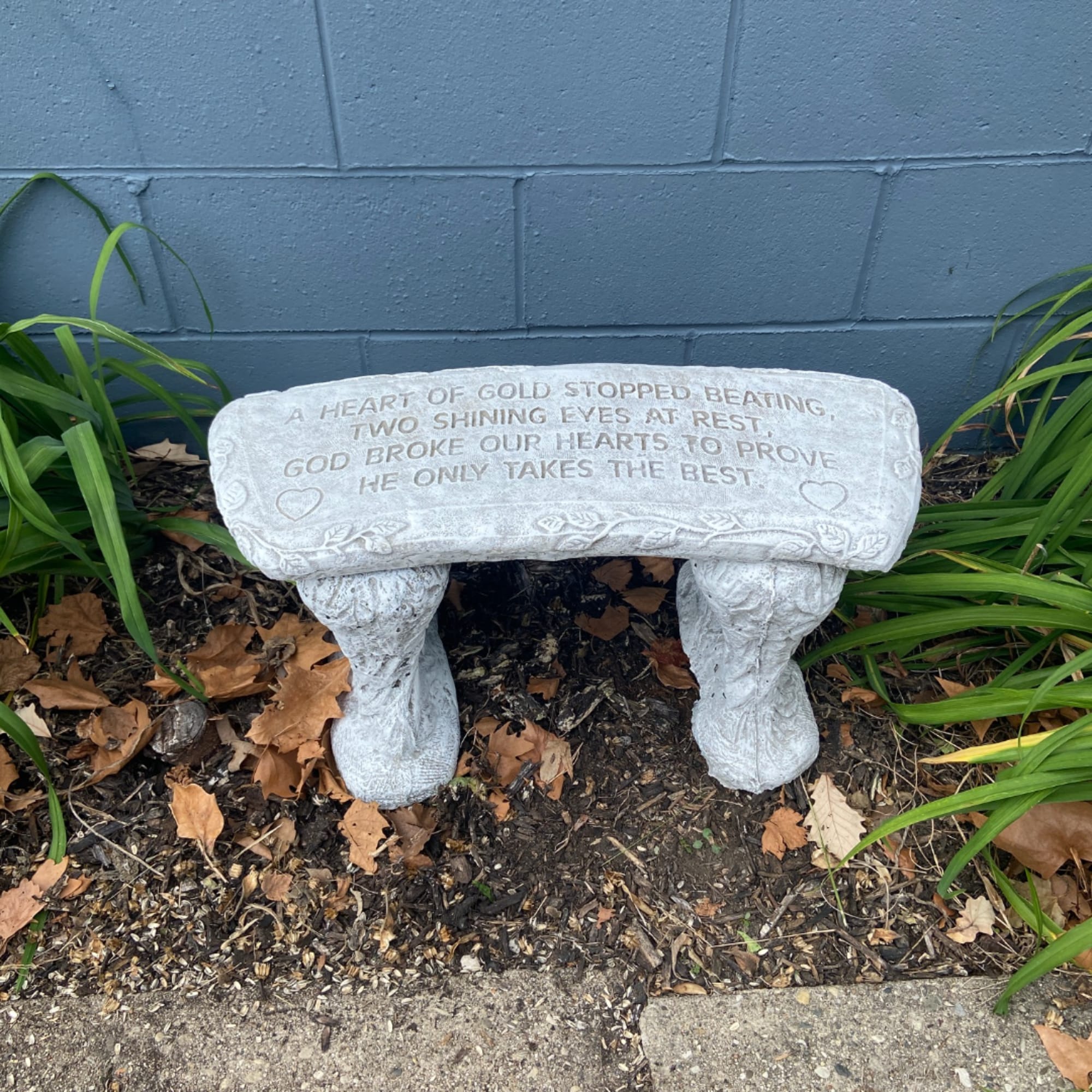 Stone memorial bench with an engraved sympathy verse in a garden bed.
