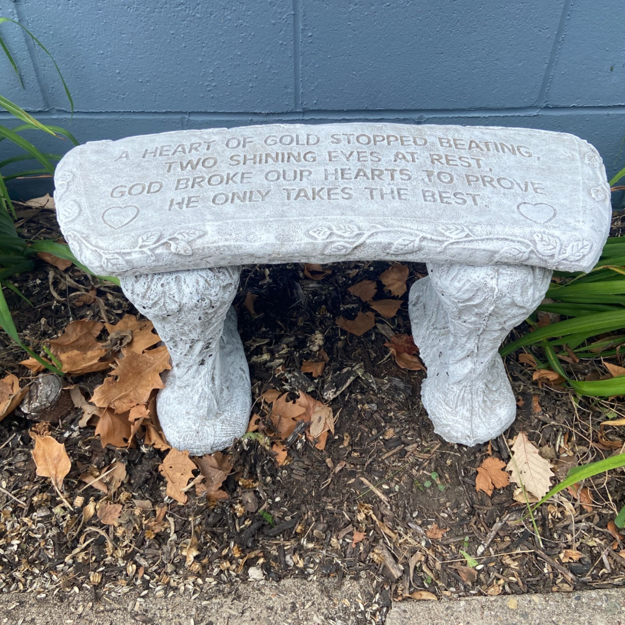 White memorial bench with an engraved tribute in a garden bed