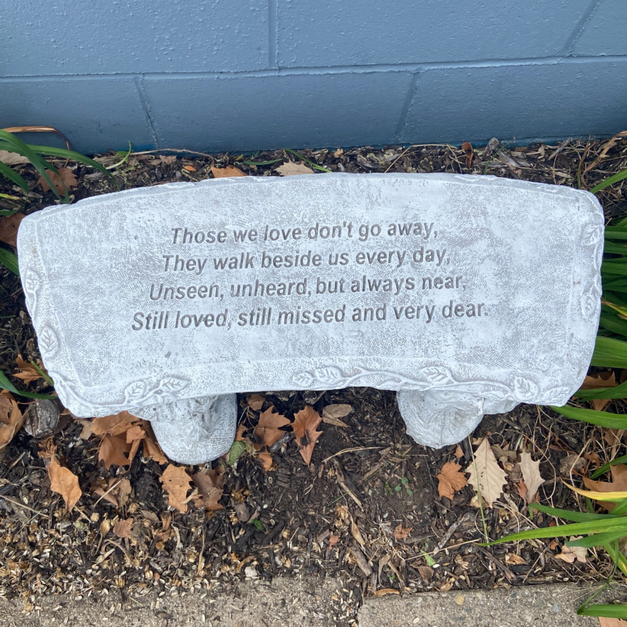 Memorial stone with a sympathy quote in a garden bed