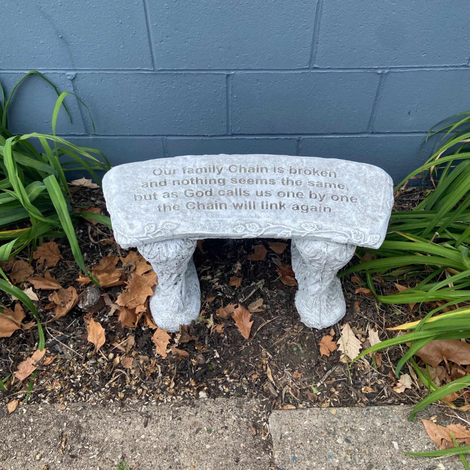 White memorial bench with engraved text in a garden bed